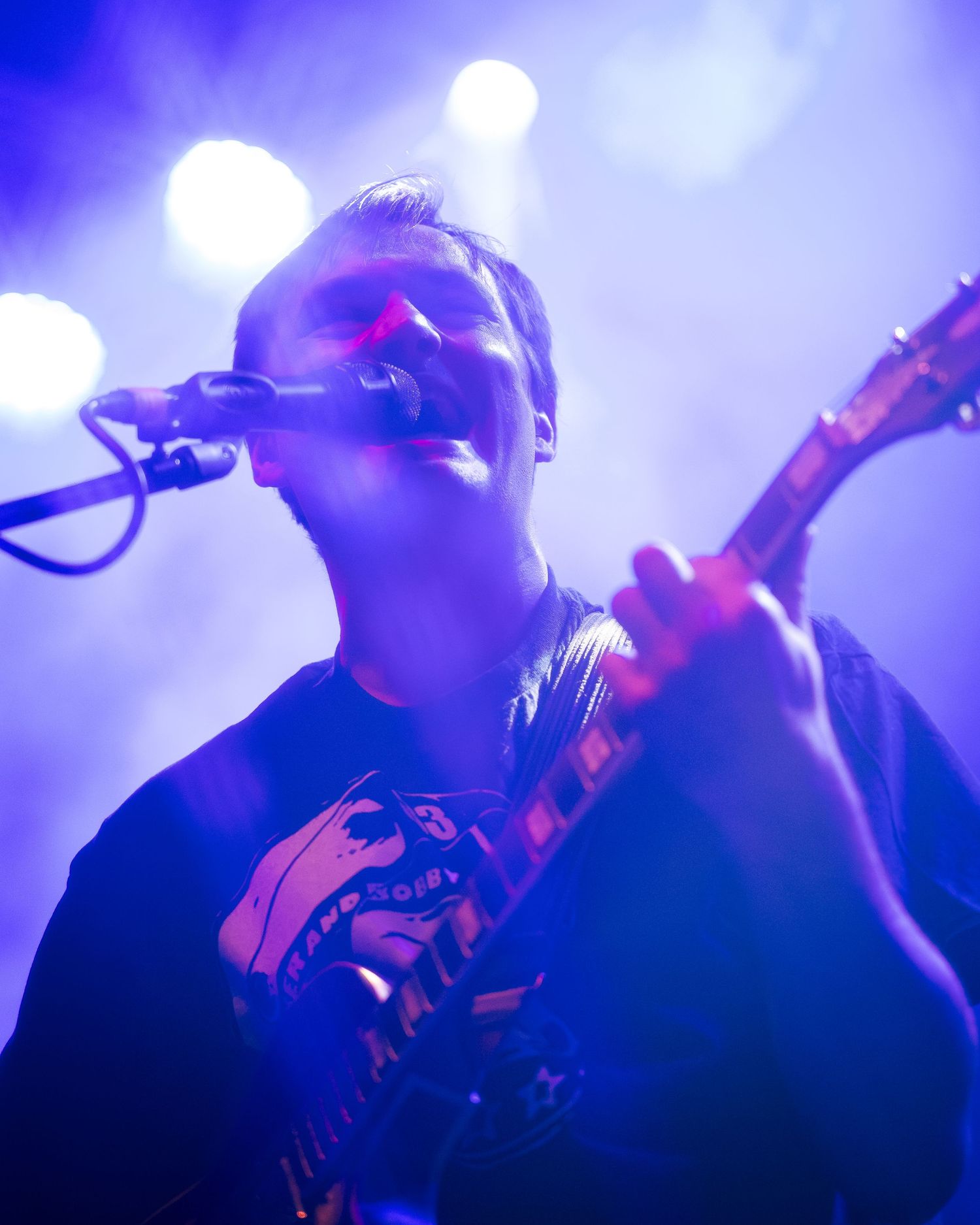 Concert performer singing and playing guitar under blue stage lighting.