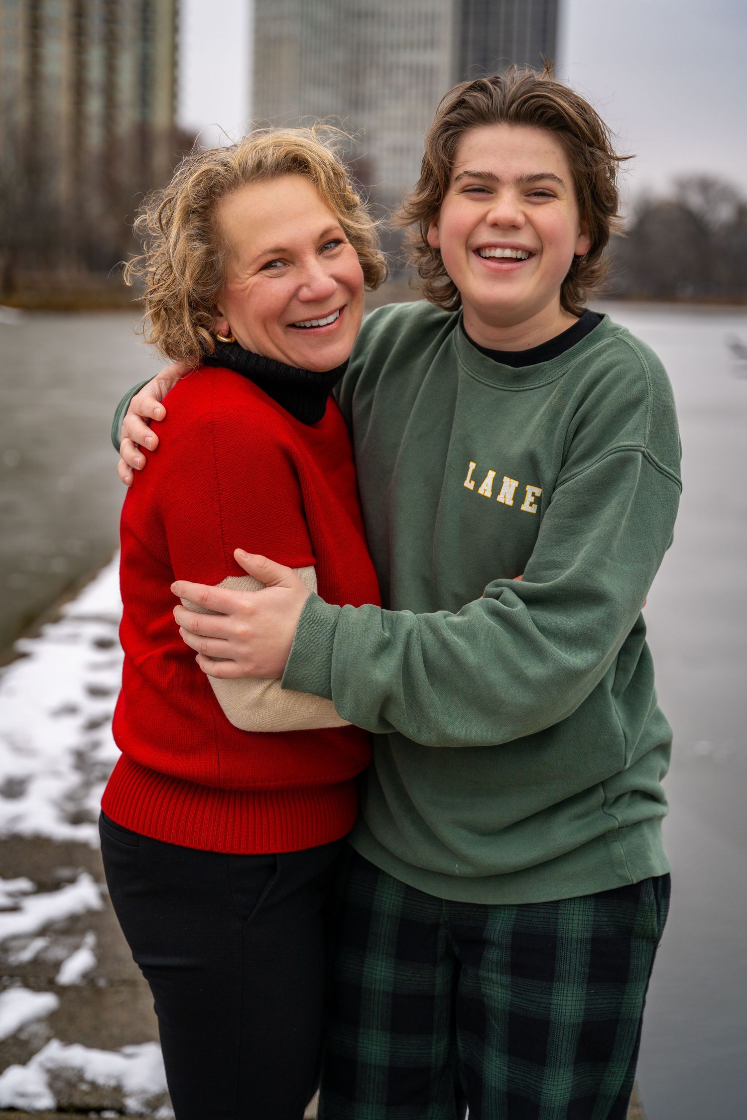 Two people in sweaters share warm embraces and laughter in a winter landscape by the water.