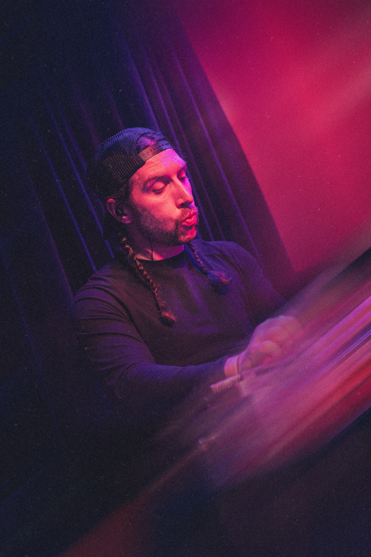 A performer sings passionately on stage bathed in dramatic purple and pink lighting during a live music performance.