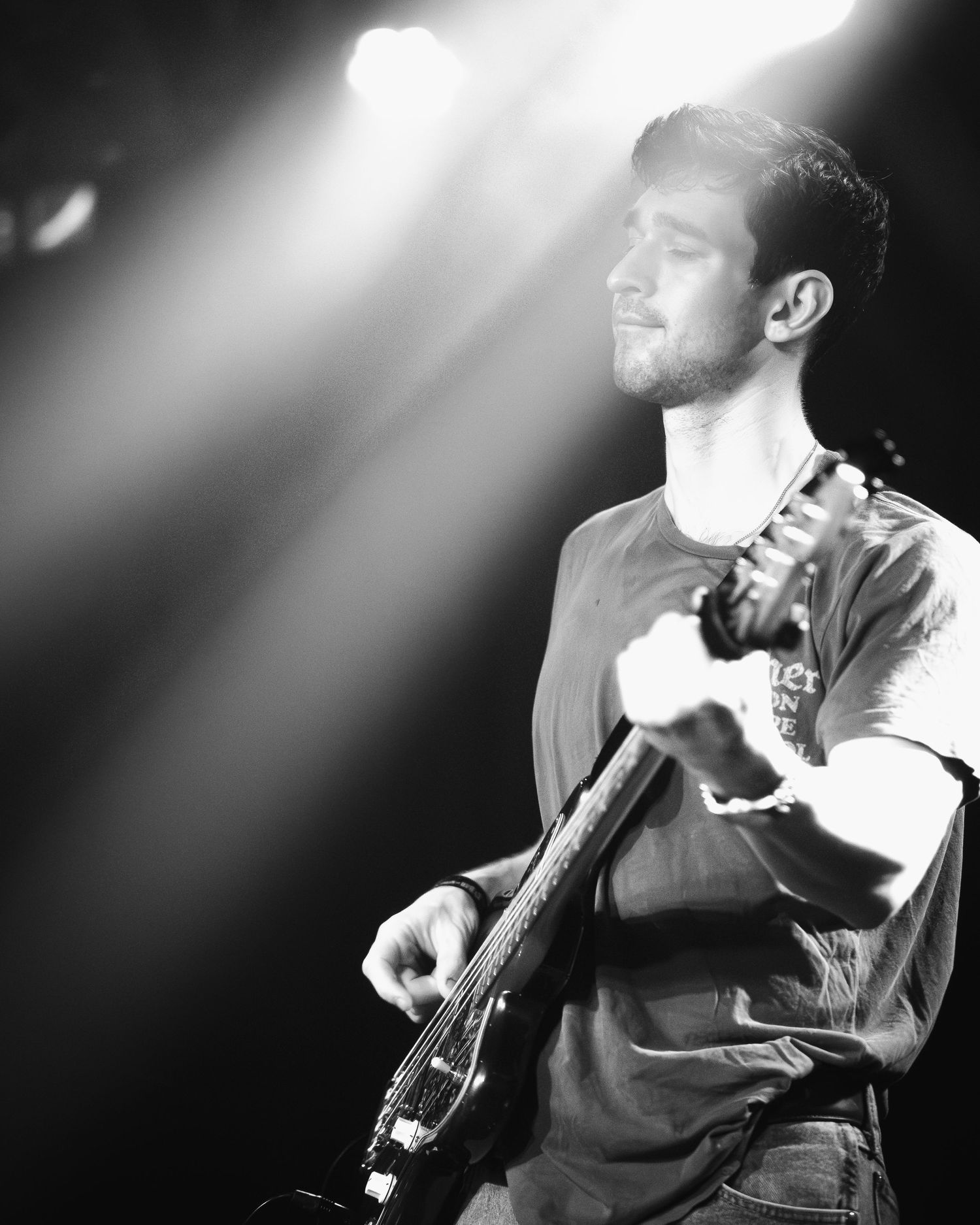 Black and white portrait of musician playing bass guitar in dramatic stage lighting.