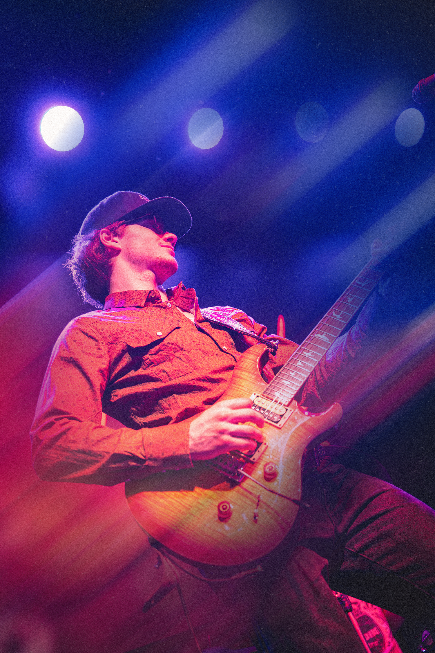 Guitar player performs on stage under dramatic blue and red concert lighting with electric guitar.