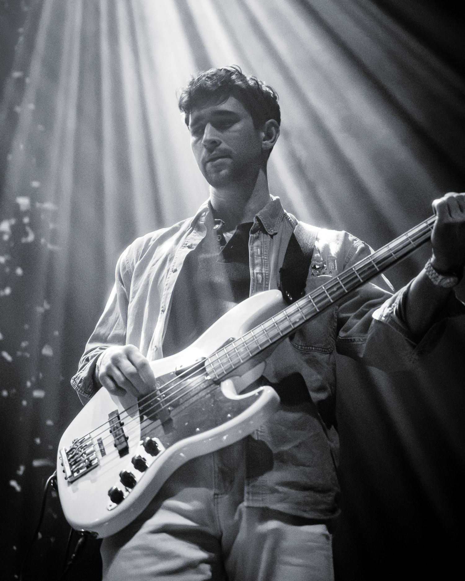 Musician playing white bass guitar under dramatic stage lighting in black and white photo.