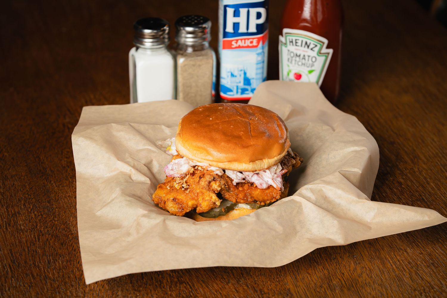 Chicken sandwich served on brown paper with condiments and salt shakers.