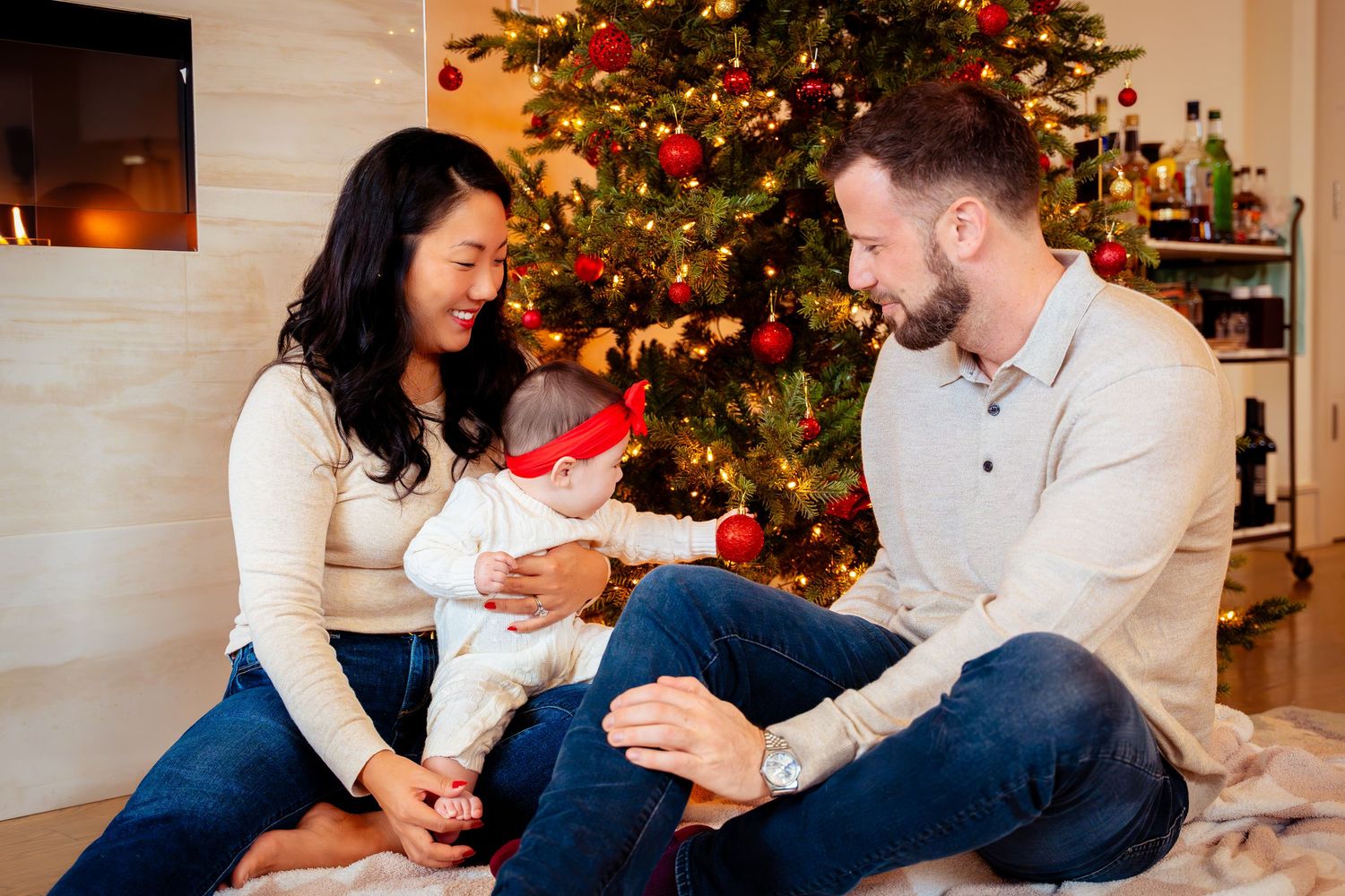 A family sits together by a decorated Christmas tree in their living room sharing a warm holiday moment.