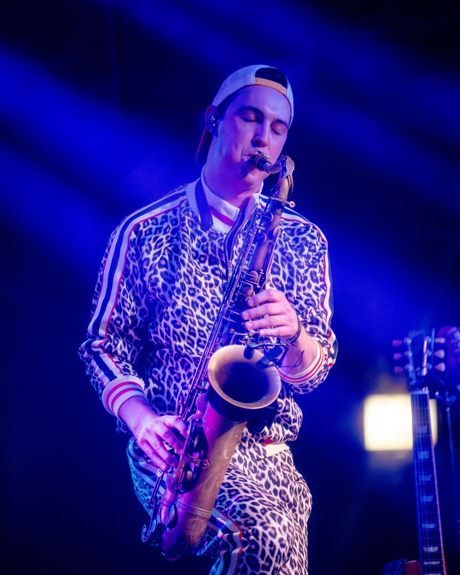 Musician in leopard print shirt plays instrument under blue concert lighting.
