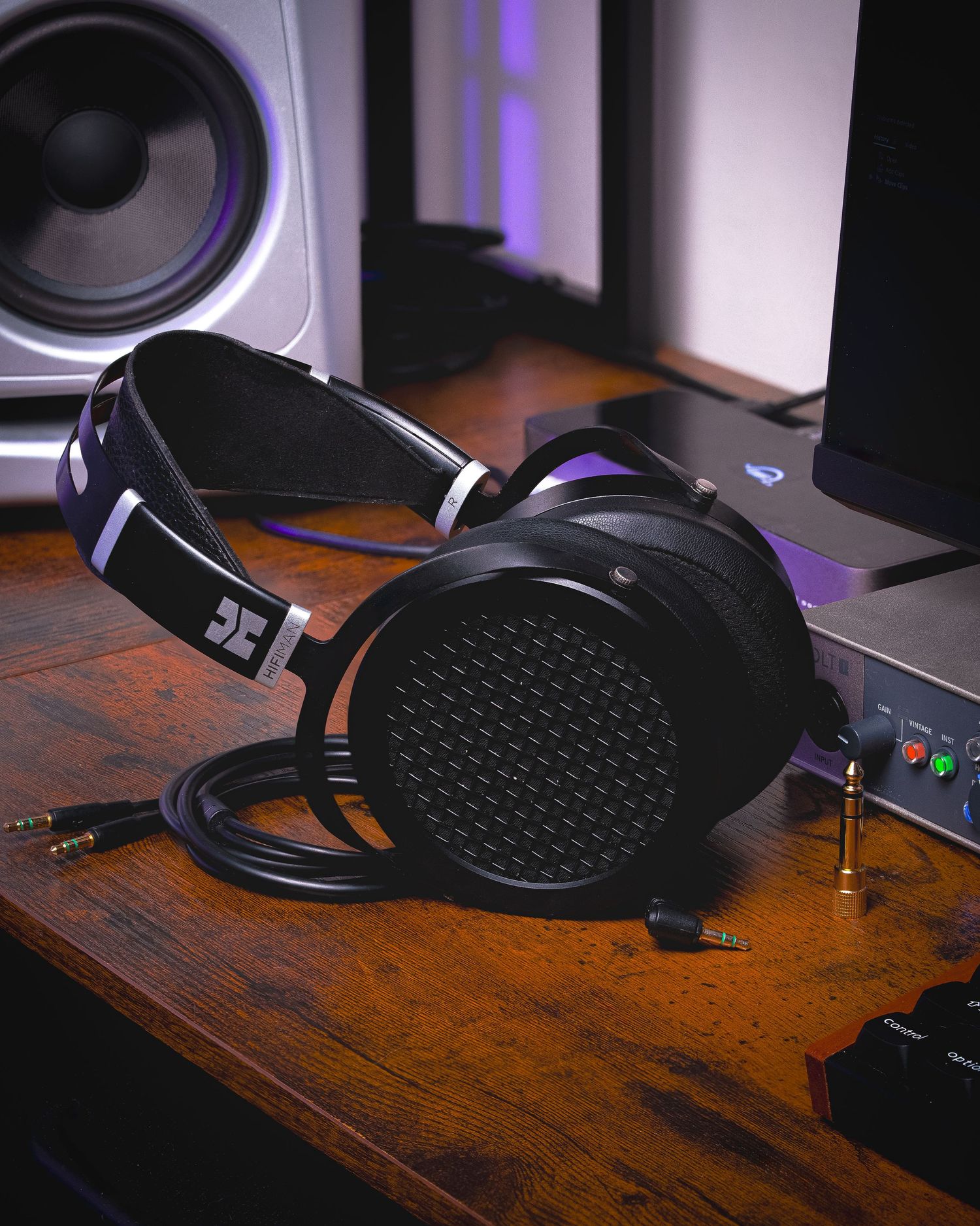 Black audiophile headphones on wooden desk with purple ambient lighting in background.