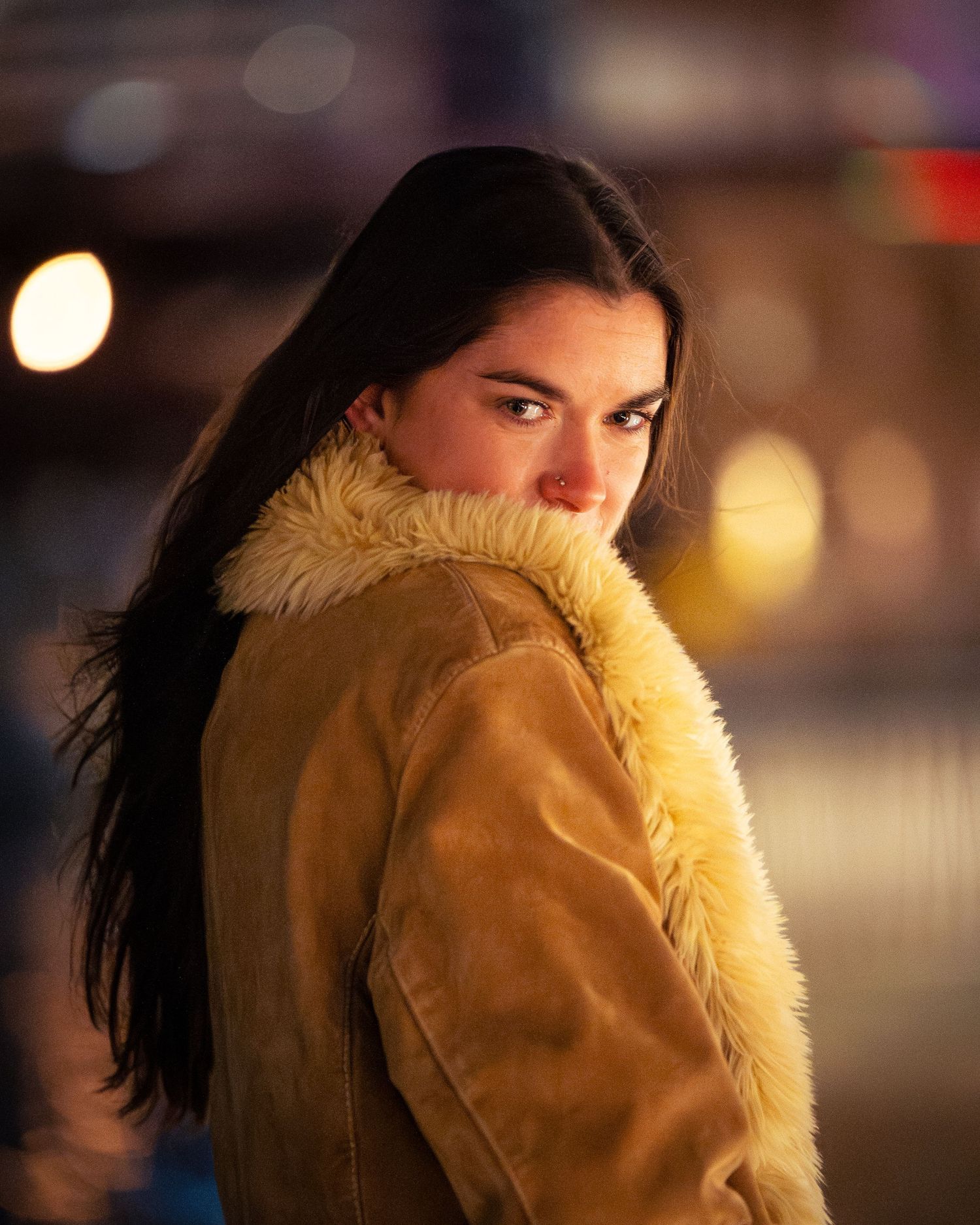 Side profile view of someone wearing a tan fur-trimmed coat against a blurred evening background.