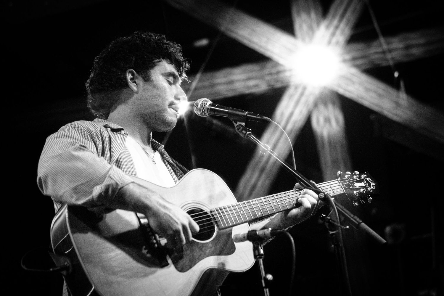 Concert performer plays acoustic guitar under dramatic stage lighting during live show.