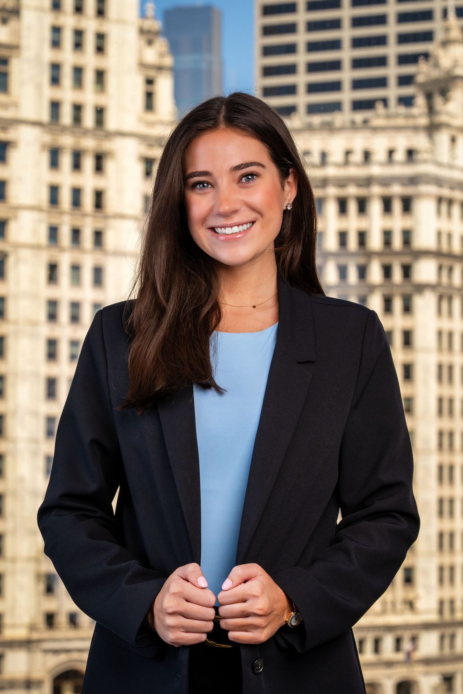 Corporate headshots featuring dark blazer and blue top with urban architecture in background.