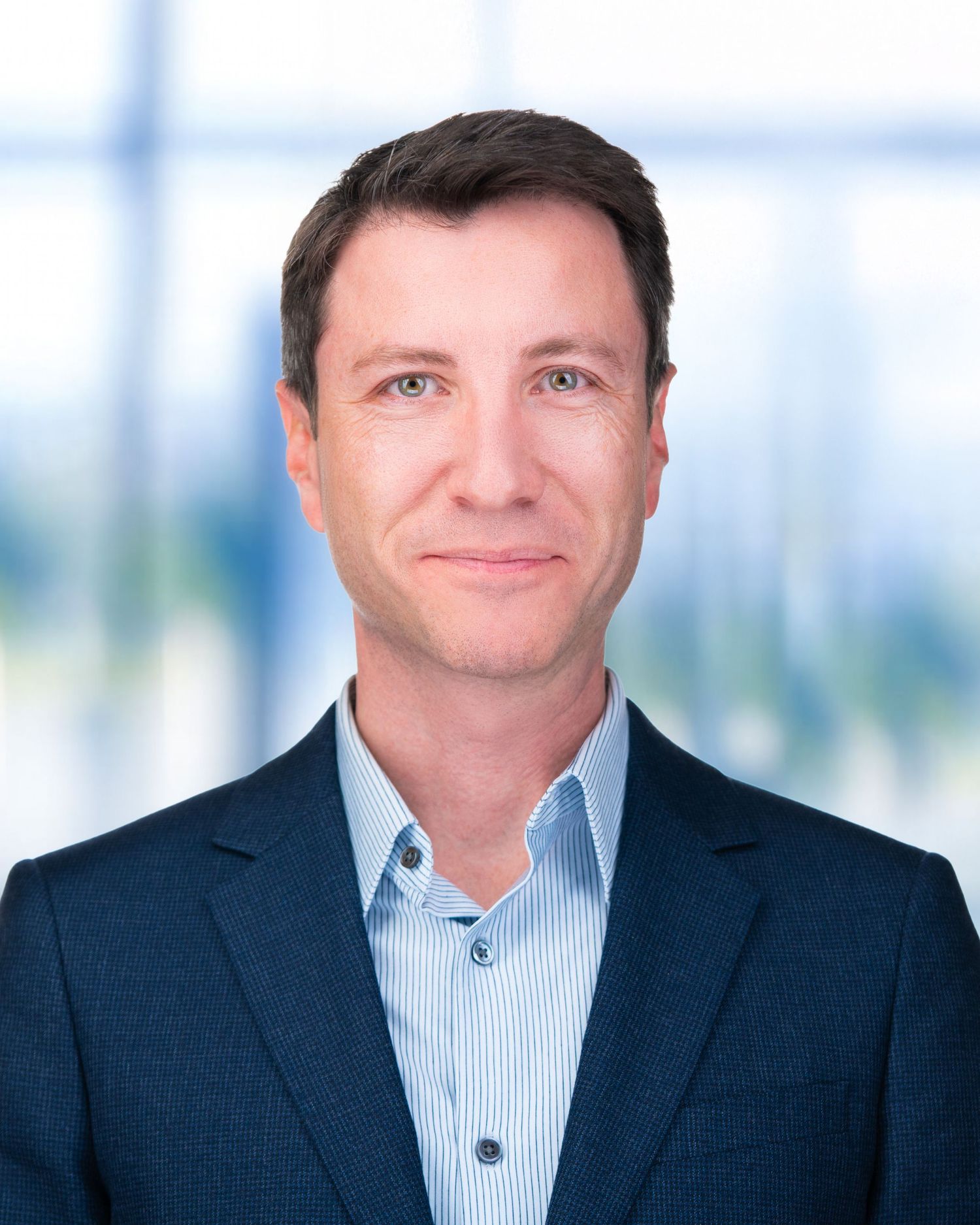 Business headshot of person wearing striped dress shirt and navy blazer with bright backdrop.