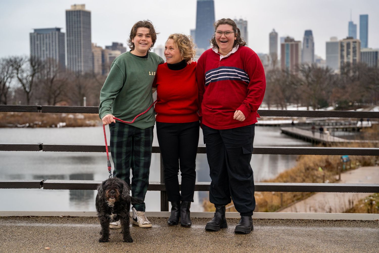 A group in red and green sweaters poses along a waterfront railing with the Chicago skyline visible in the background.