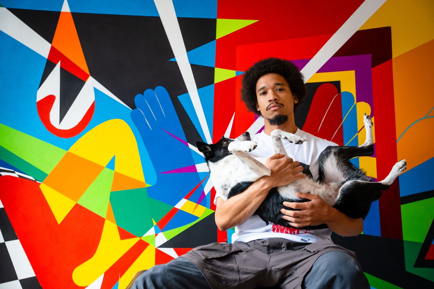Person posing expressively against vibrant geometric colorful wall mural background.