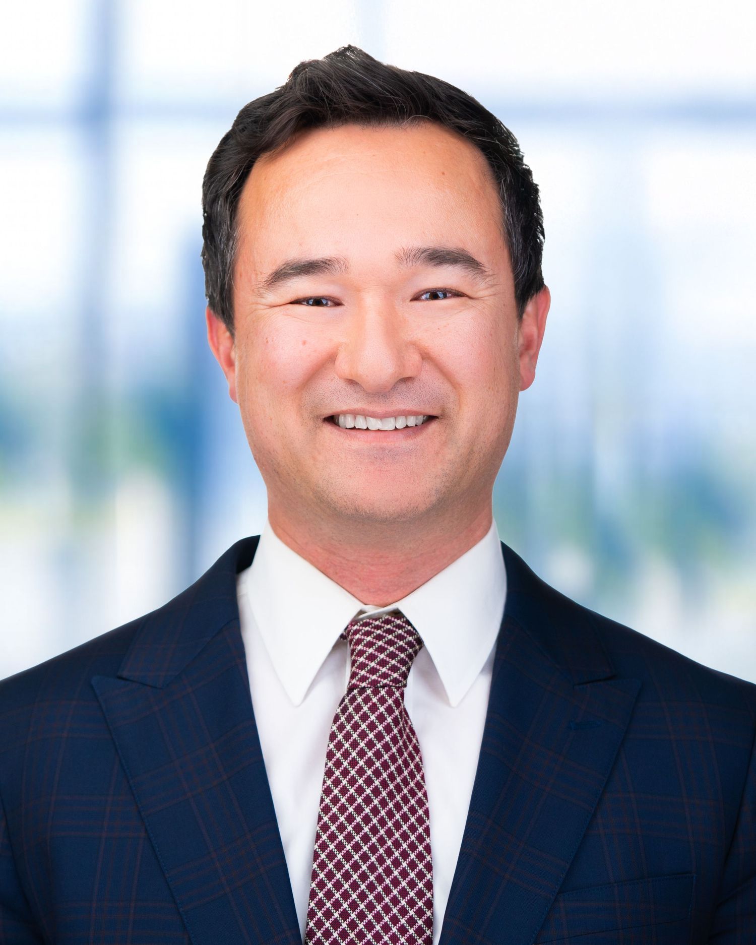 Executive portrait of person in navy suit and patterned tie against bright office setting.