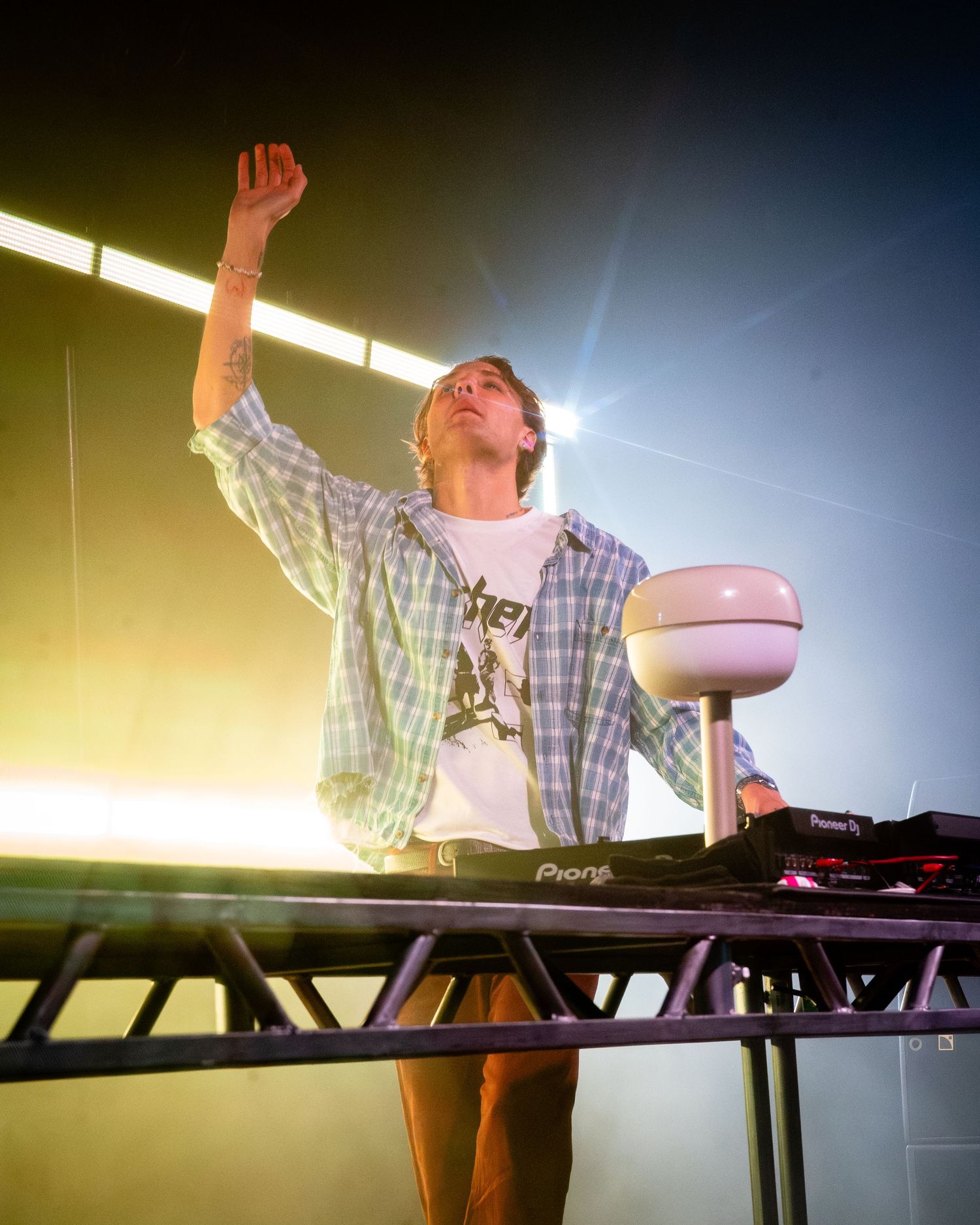 Musician performing at electronic music setup with raised arm and dramatic lighting.