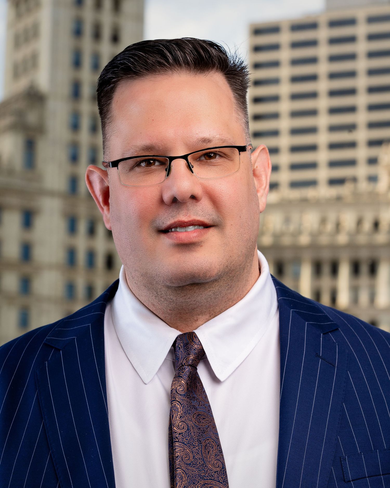 Executive portraits in pinstripe suit and glasses against urban backdrop.