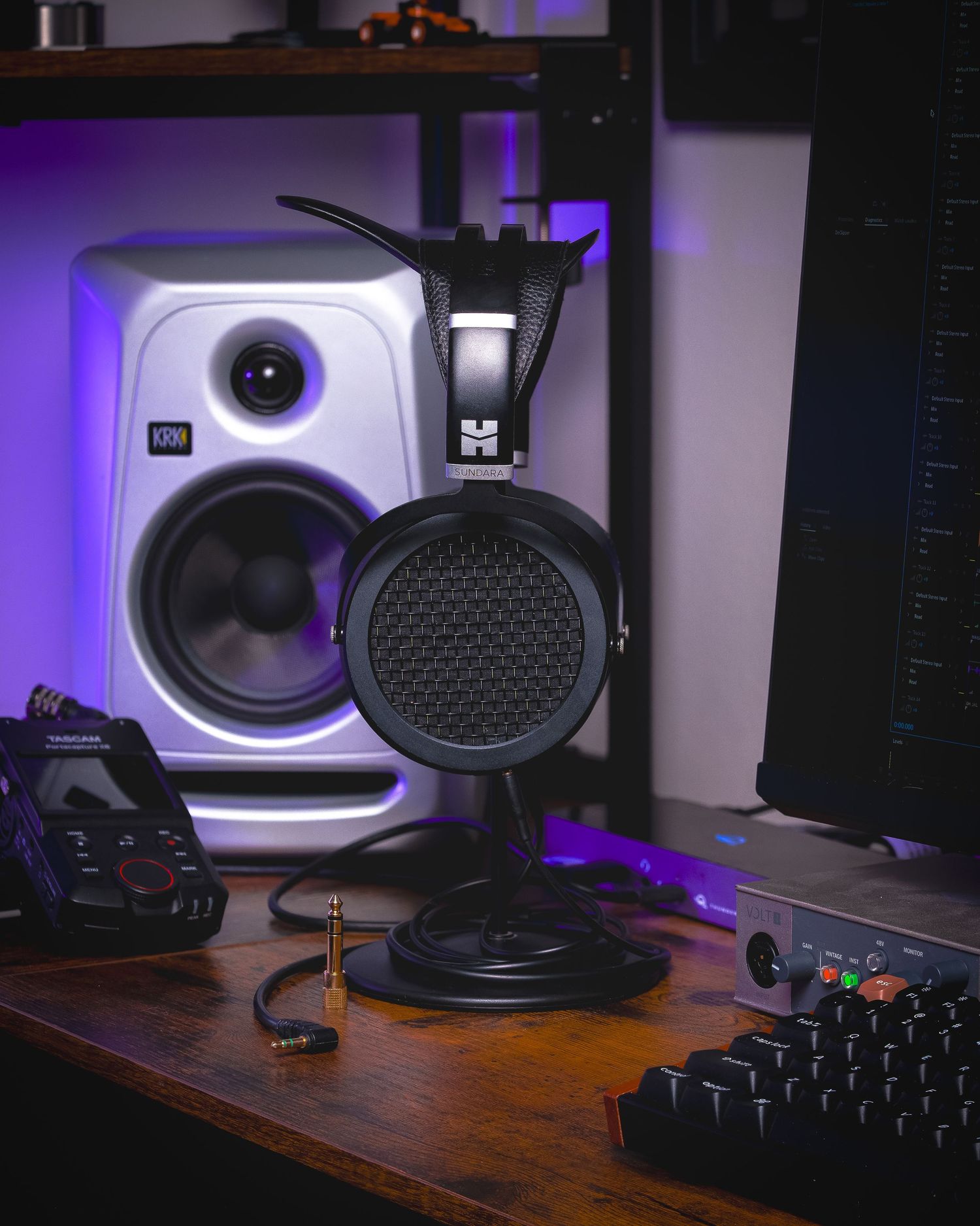 Studio monitor speakers and gaming controller on wooden desk with purple ambient lighting in background.