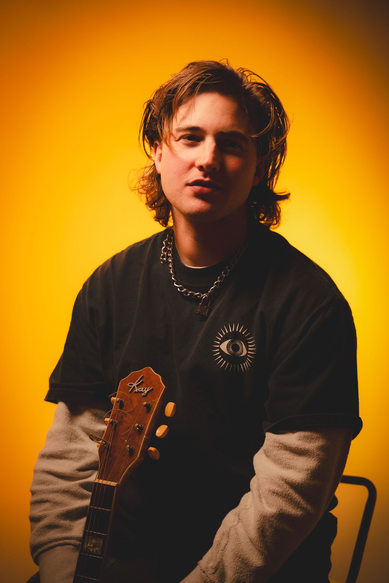 Artist with acoustic guitar photographed against vibrant orange background in moody lighting setup.