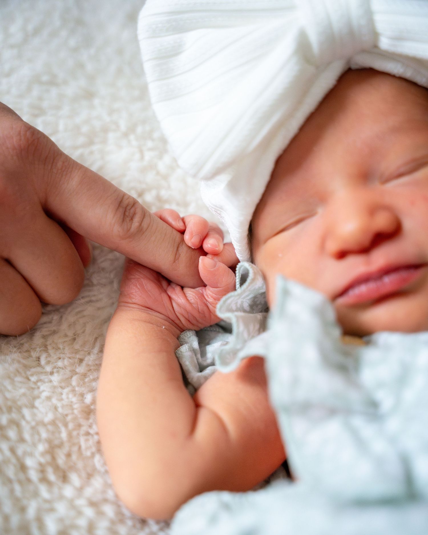 Peaceful sleeping baby dressed in white lace outfit on textured blanket.