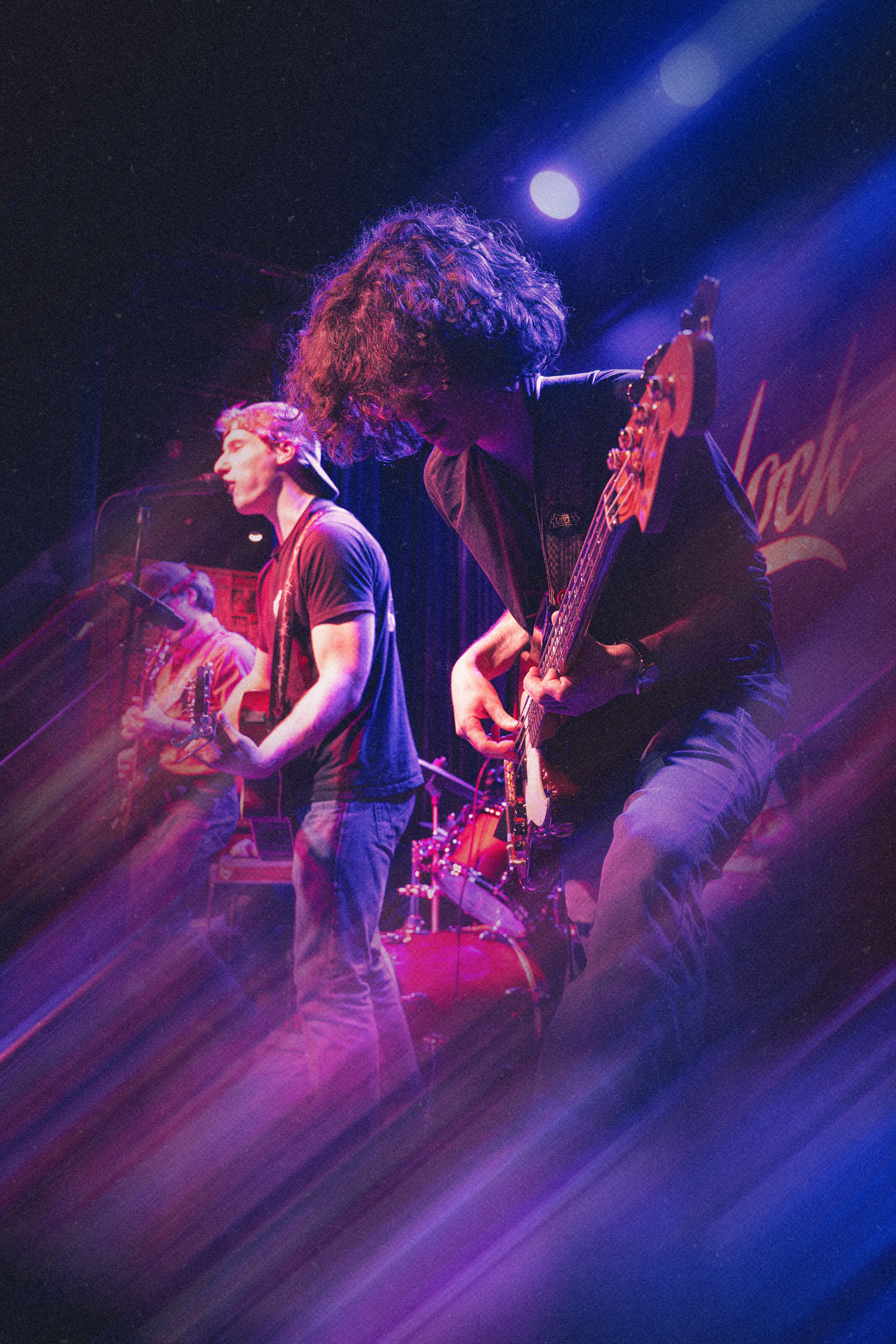Rock band performs energetically on stage with dramatic blue and purple lighting effects during live concert performance.
