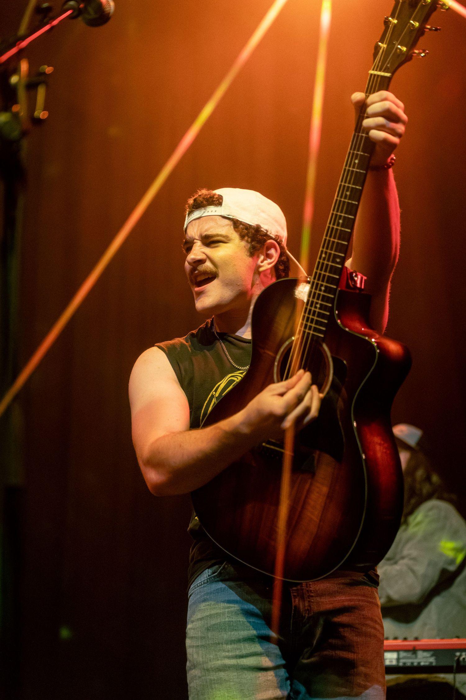 Performer singing and playing acoustic guitar under warm orange stage lighting.