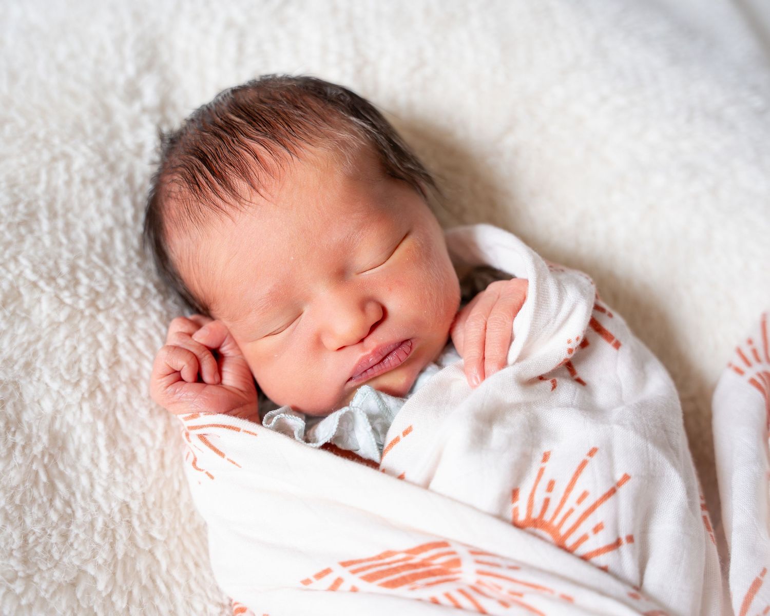 Peaceful newborn baby sleeping soundly on white blanket in soft natural lighting.