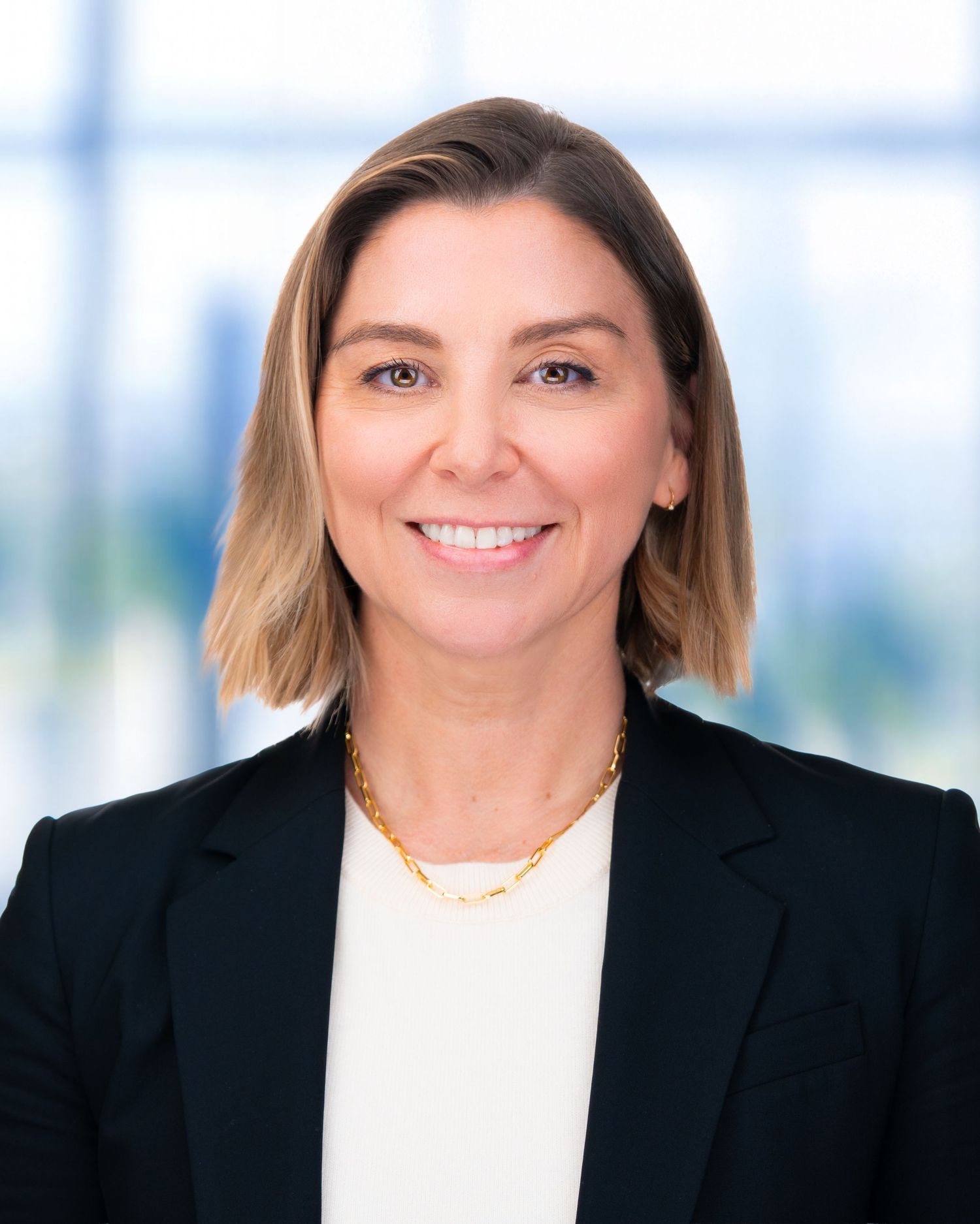Business portrait of person in black blazer and white top against bright modern office background.