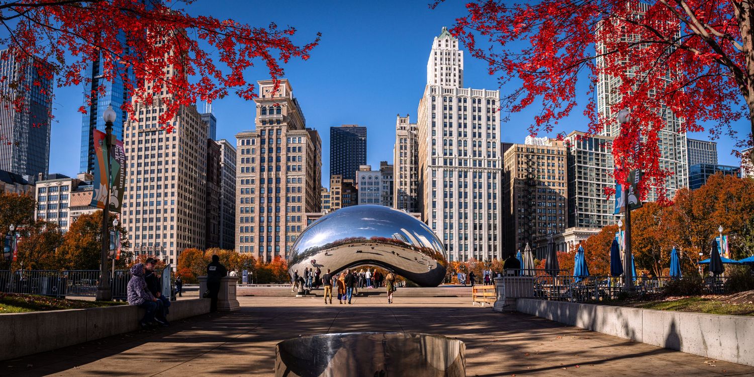 Panoramic view of Chicago skyline with red autumn trees and Cloud Gate sculpture in Millennium Park.