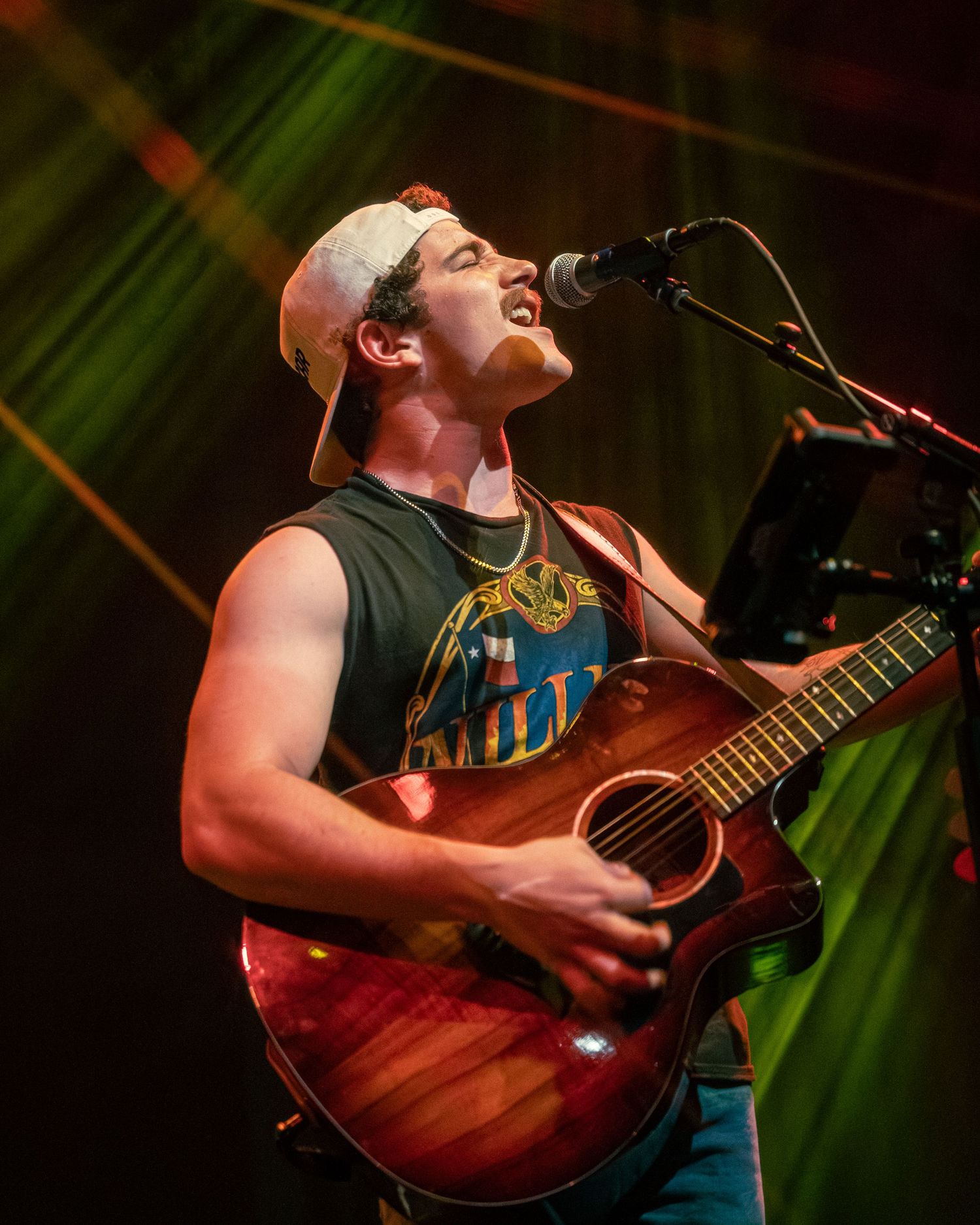 Musician performing with acoustic guitar under dramatic green stage lighting.