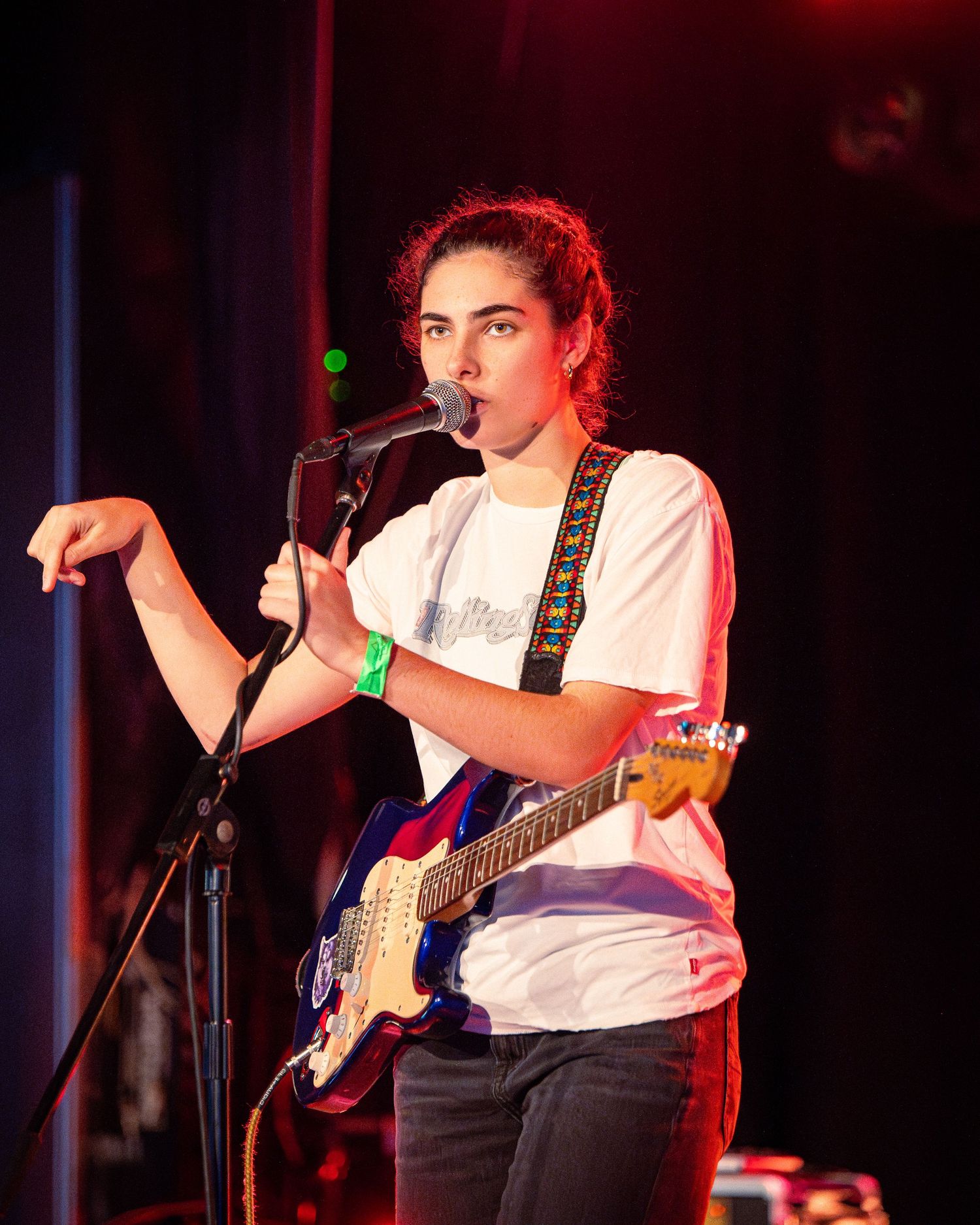 Singer performs with guitar on dimly lit stage with red lighting effects.