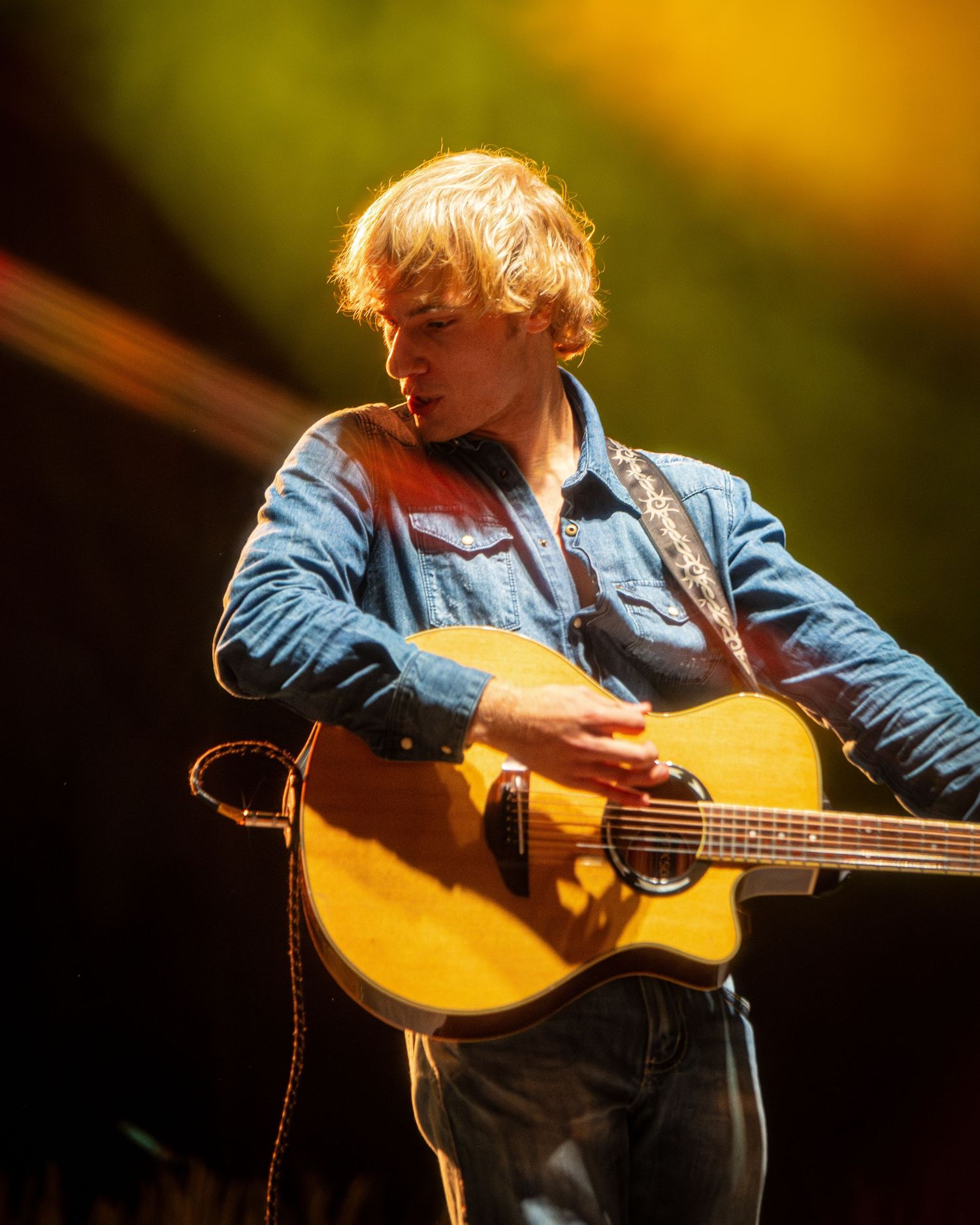 Close-up of acoustic guitar performance with denim overalls and blue jacket visible.