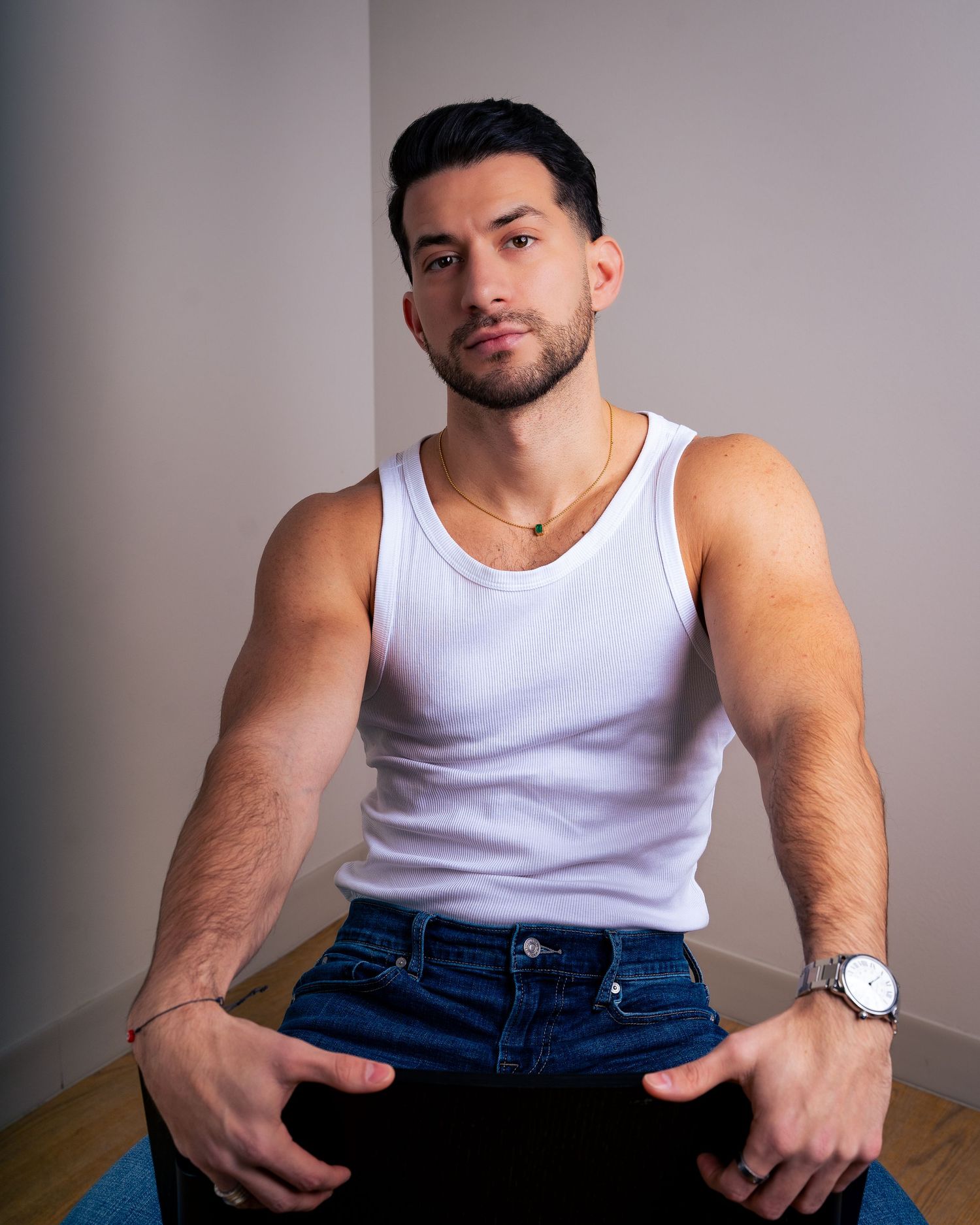 Person in sleeveless white shirt and blue jeans sits relaxed on wooden chair.