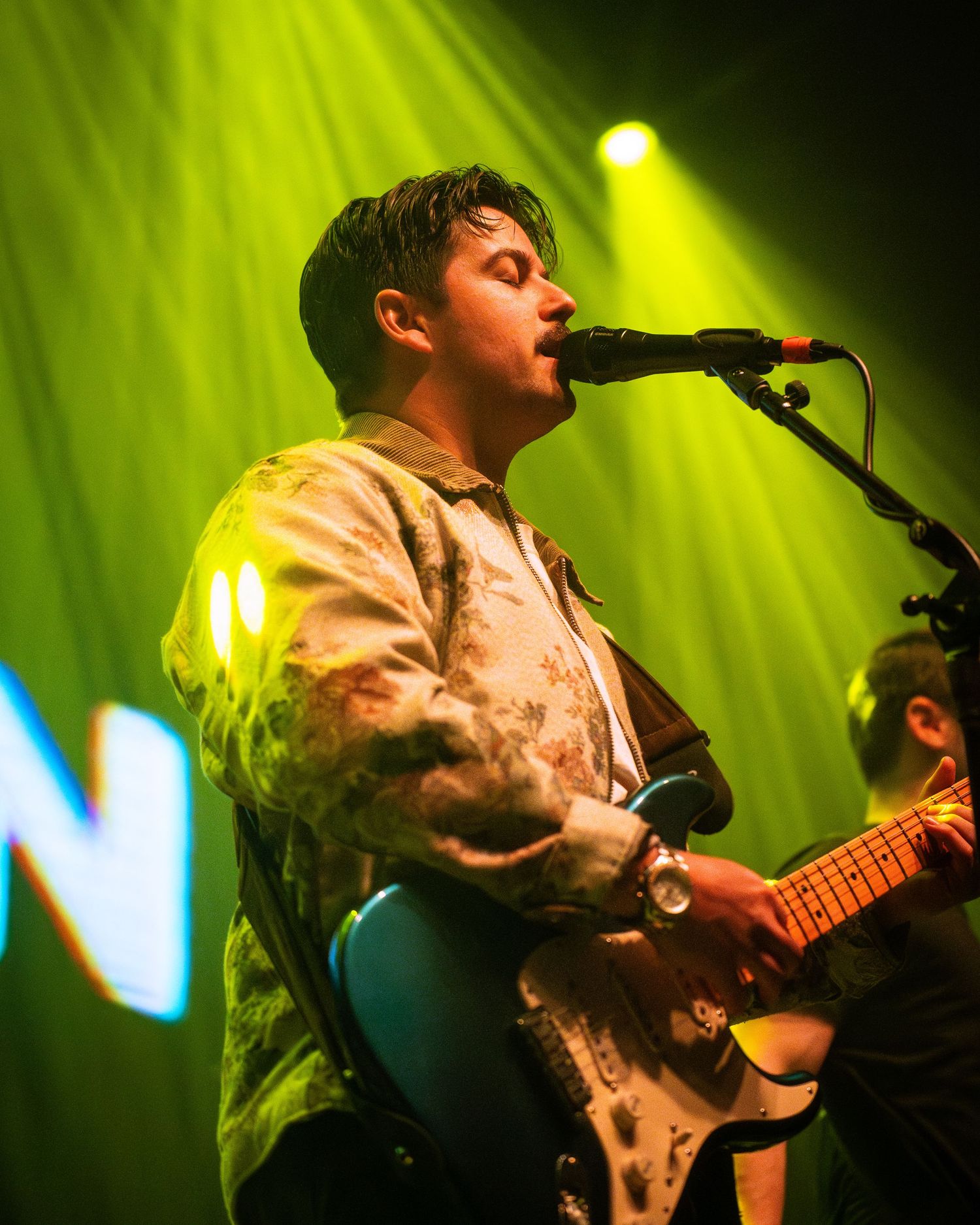 Musician performing with guitar under vibrant yellow-green stage lighting.