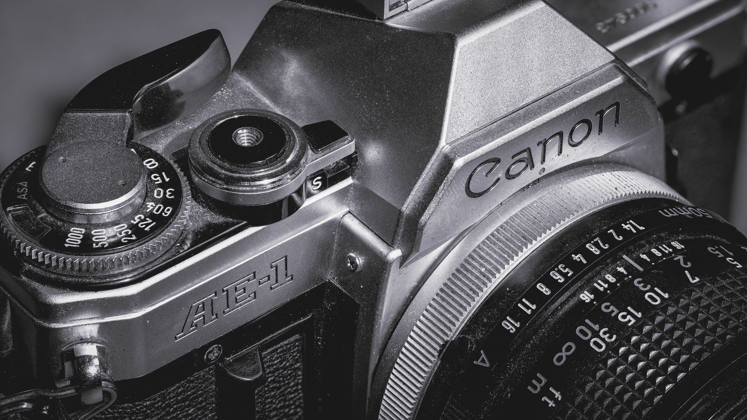 Close-up black and white detail of a vintage Canon film camera showing exposure controls and lens mount.