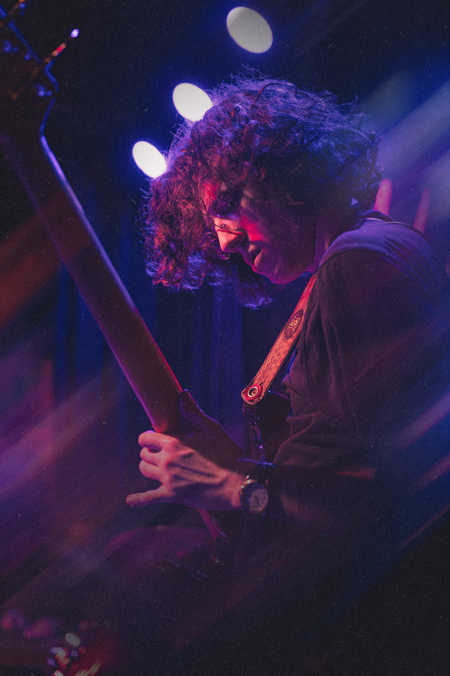 A performer plays guitar on stage bathed in dramatic blue and red lighting during a live music performance.