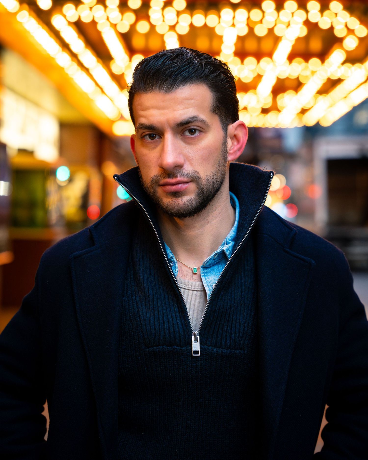 Person in navy zip-up sweater photographed against glowing carnival lights.