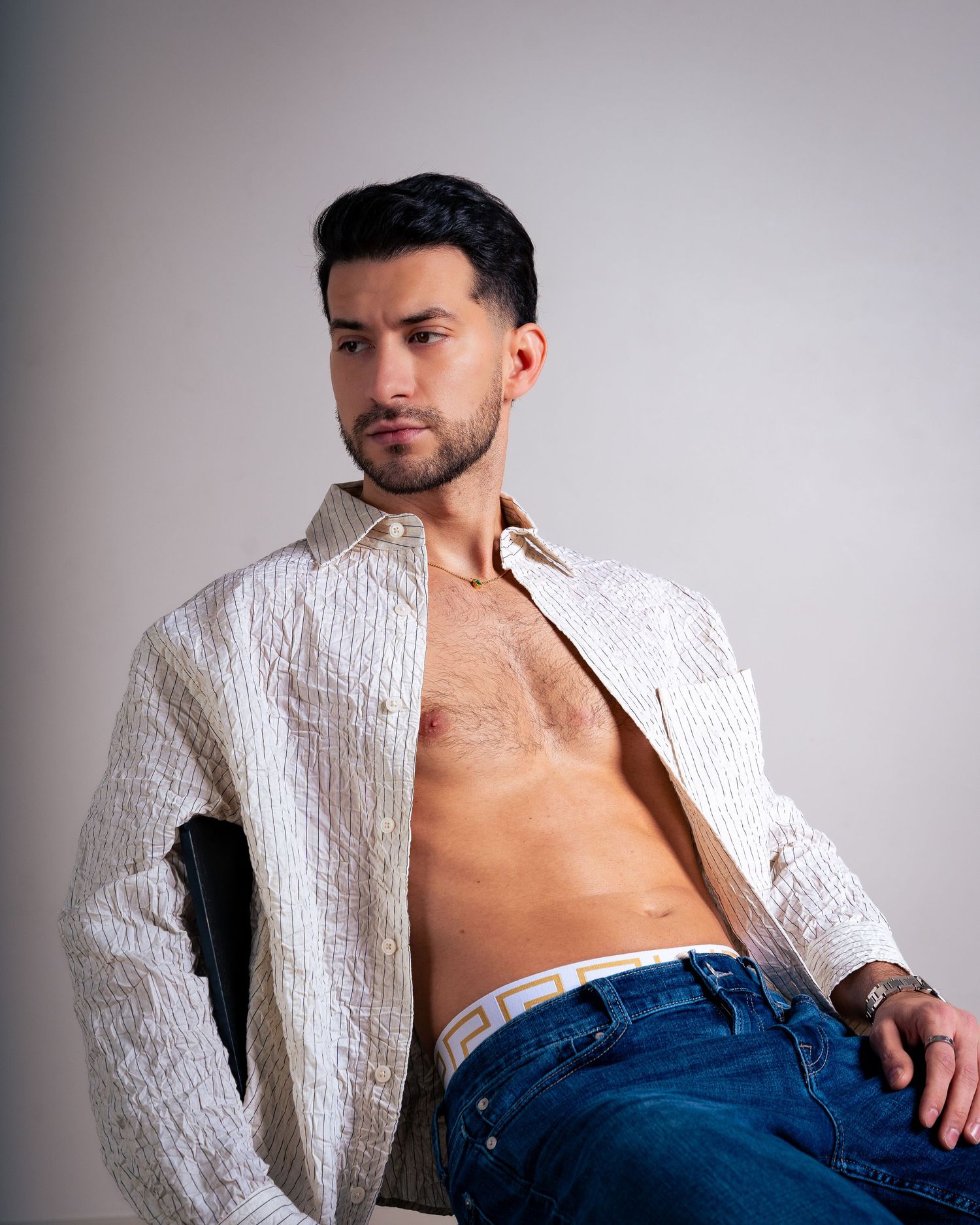 Model wearing white textured jacket with jeans in artistic studio lighting.