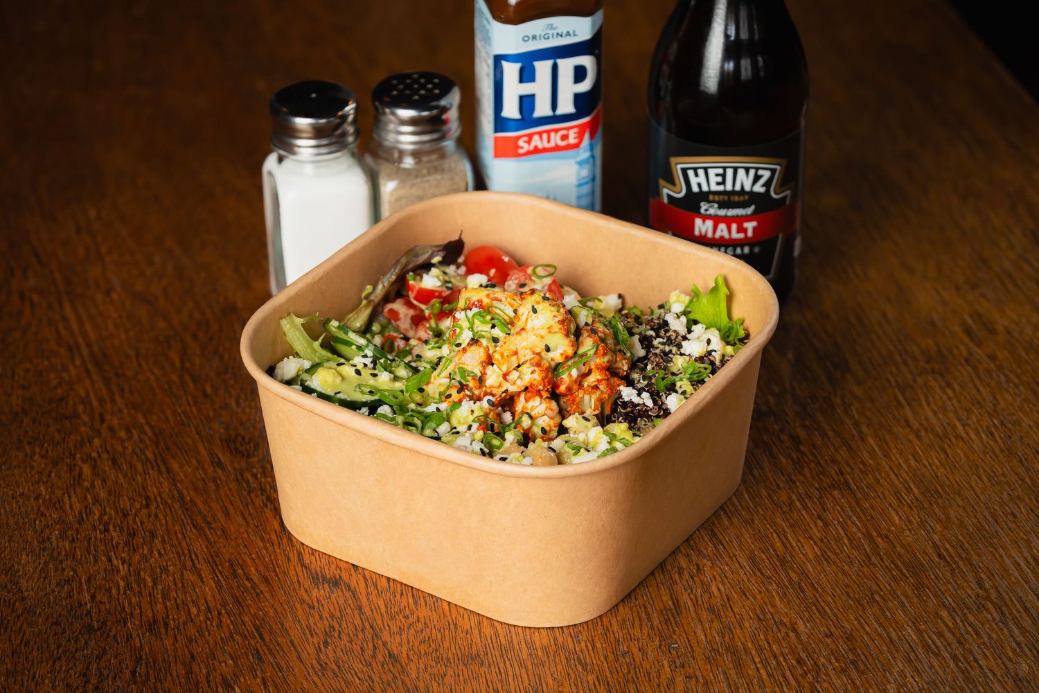 Fresh quinoa bowl with vegetables served in eco-friendly container with condiments.
