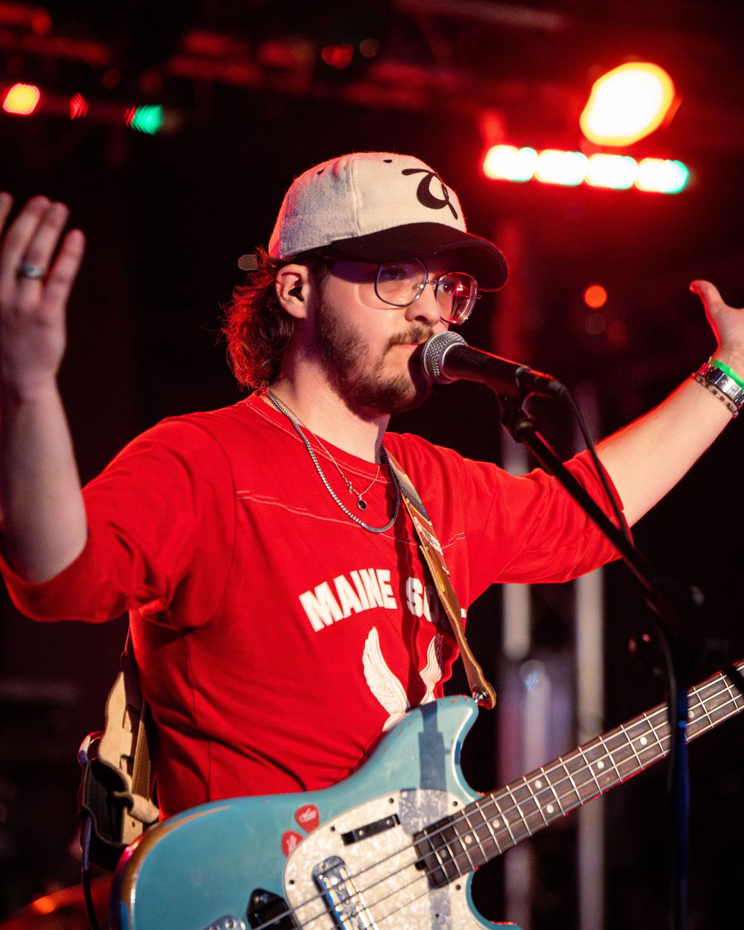Bass guitarist in red shirt performs energetically on concert stage.
