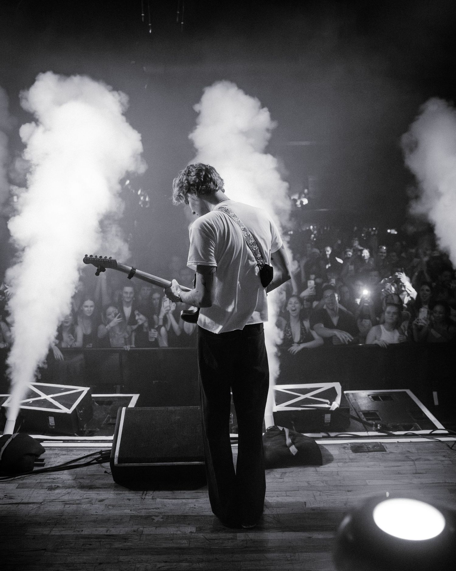 Black and white concert photo showing silhouettes of performers on stage with dramatic smoke effects.
