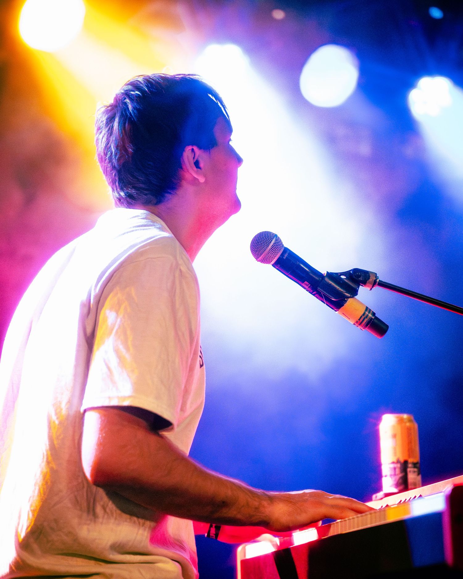 Musician performing at keyboard with colorful blue and orange stage lighting creating a dreamy atmosphere.