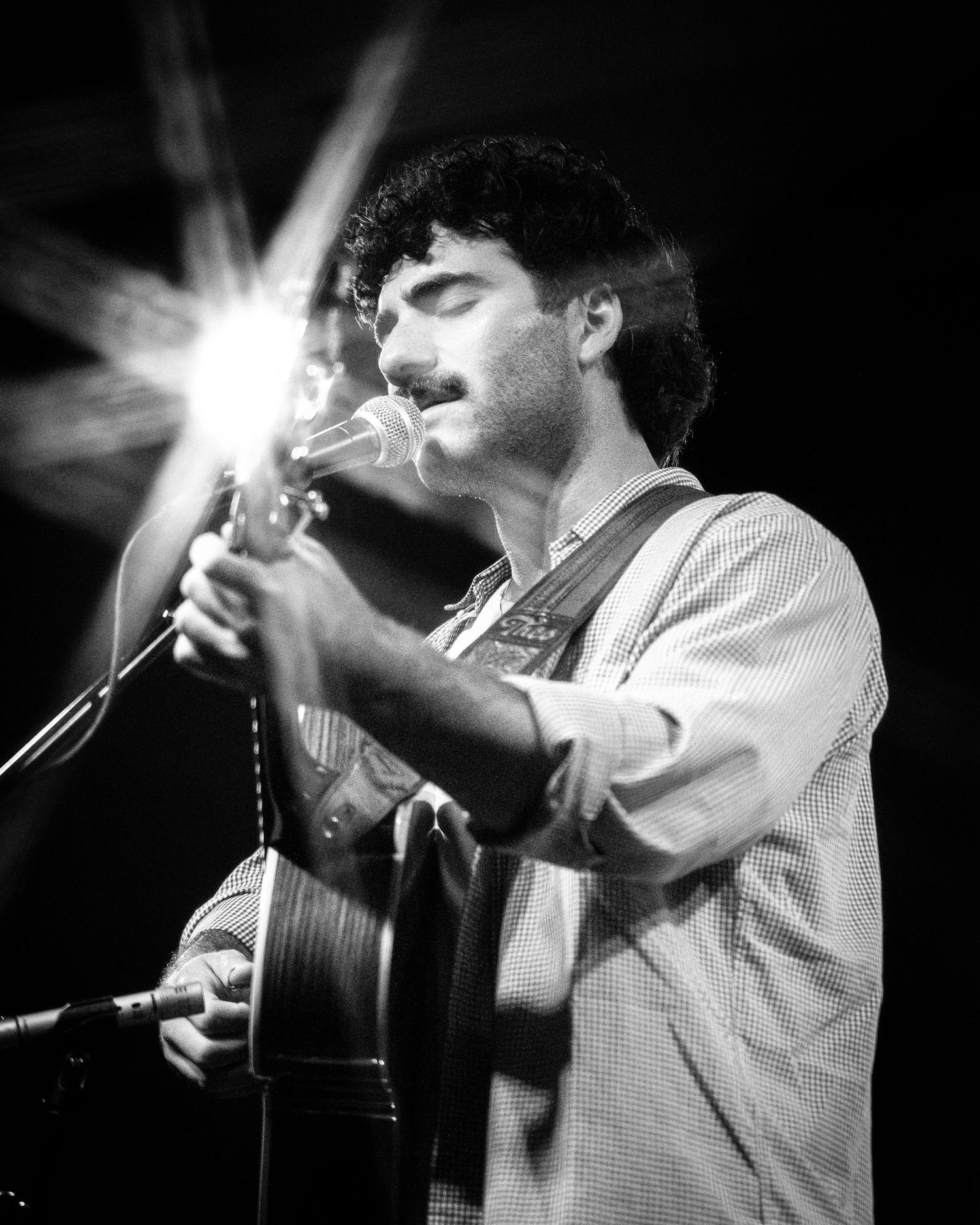 Black and white concert photo of musician playing acoustic guitar with spotlight effect.