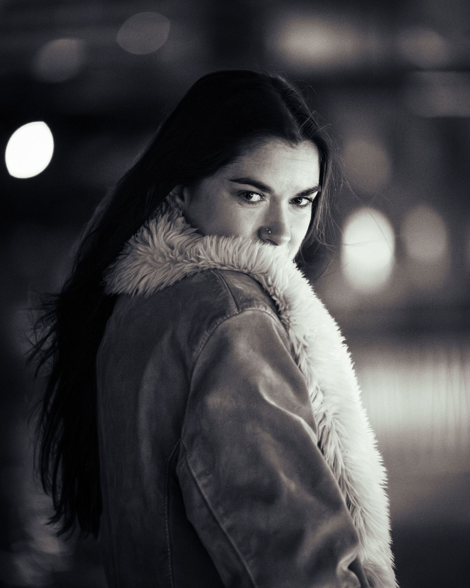 Dramatic black and white portrait showing someone in a fur coat looking over their shoulder.