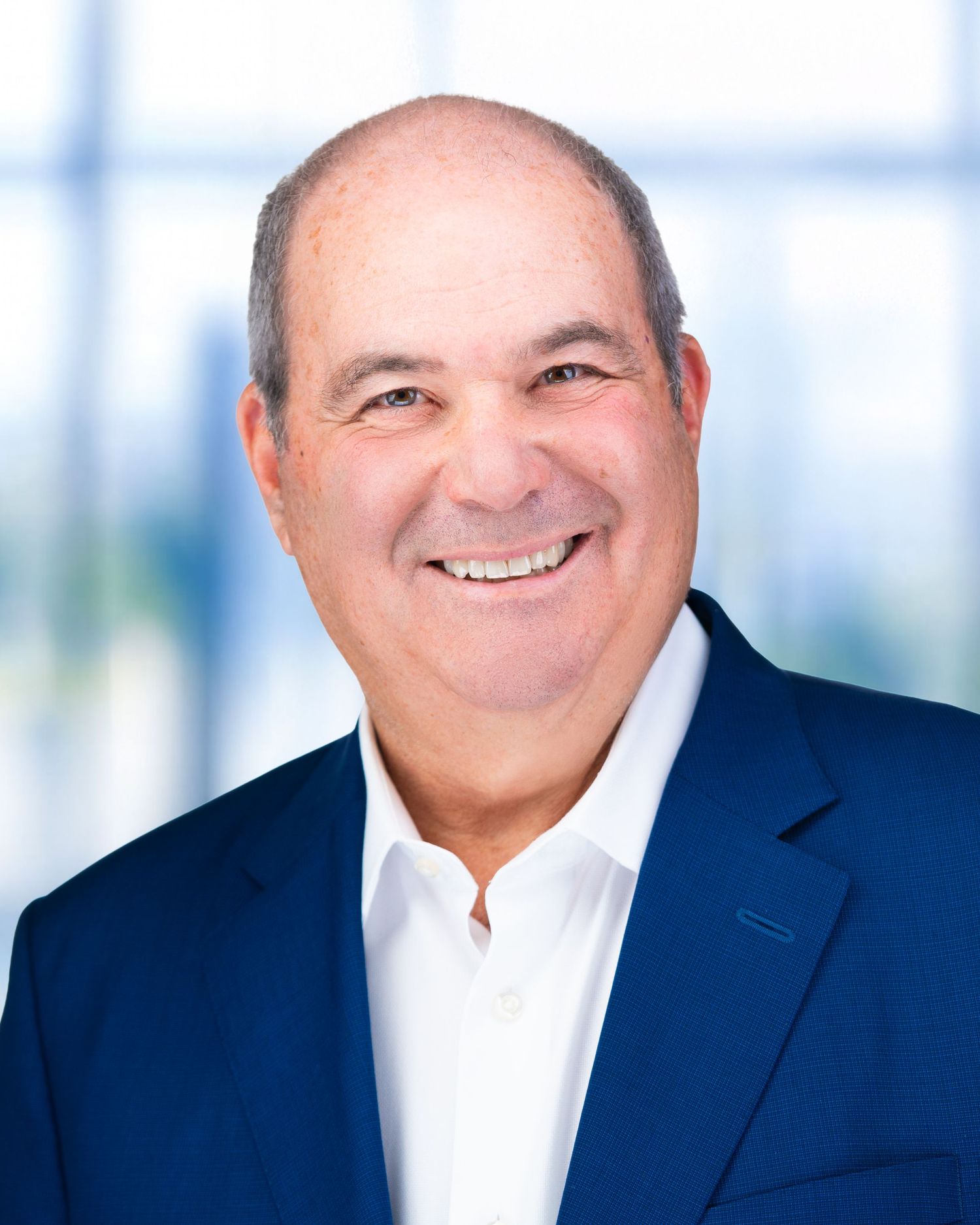 Business portrait of person in dark suit with warm smile against light office setting.