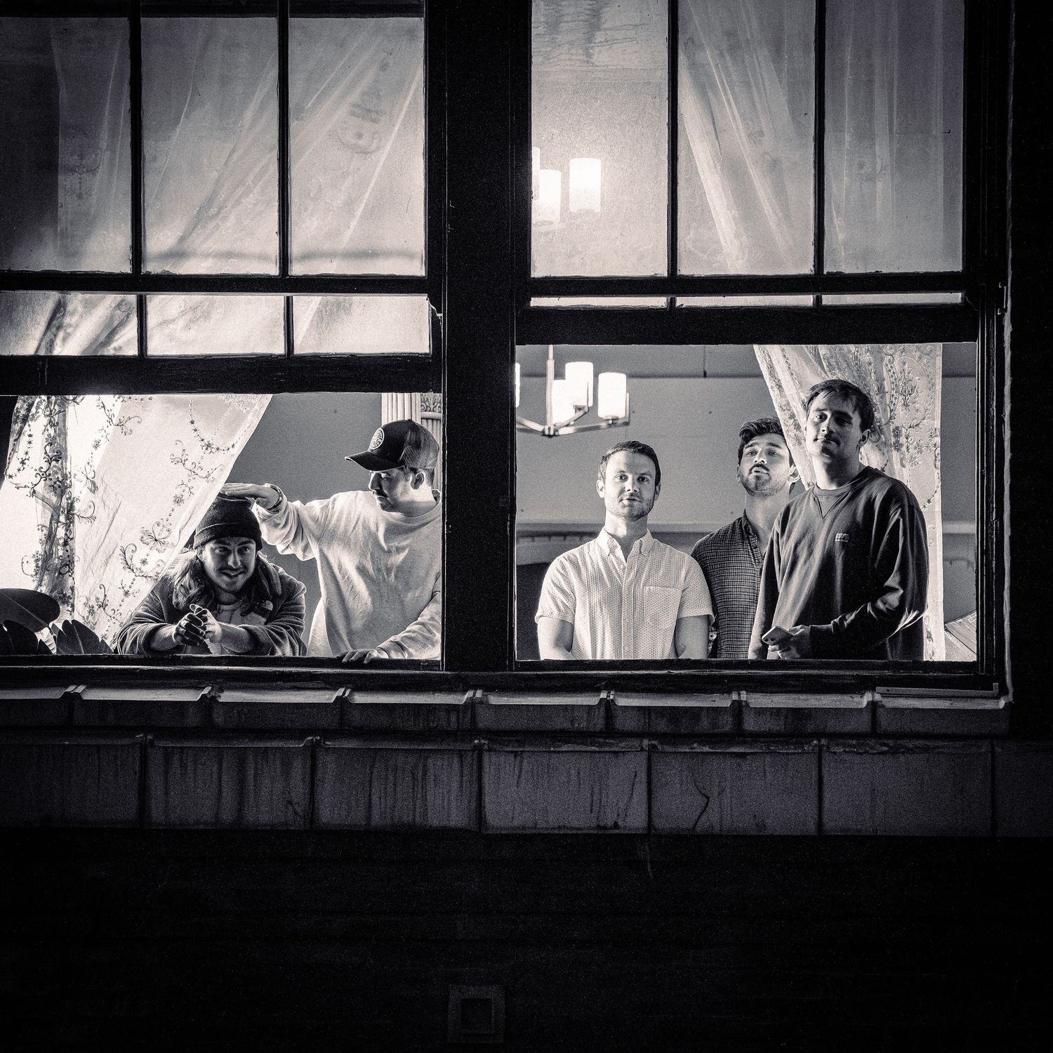 Band members stand together in a window frame for a monochrome photo shoot.