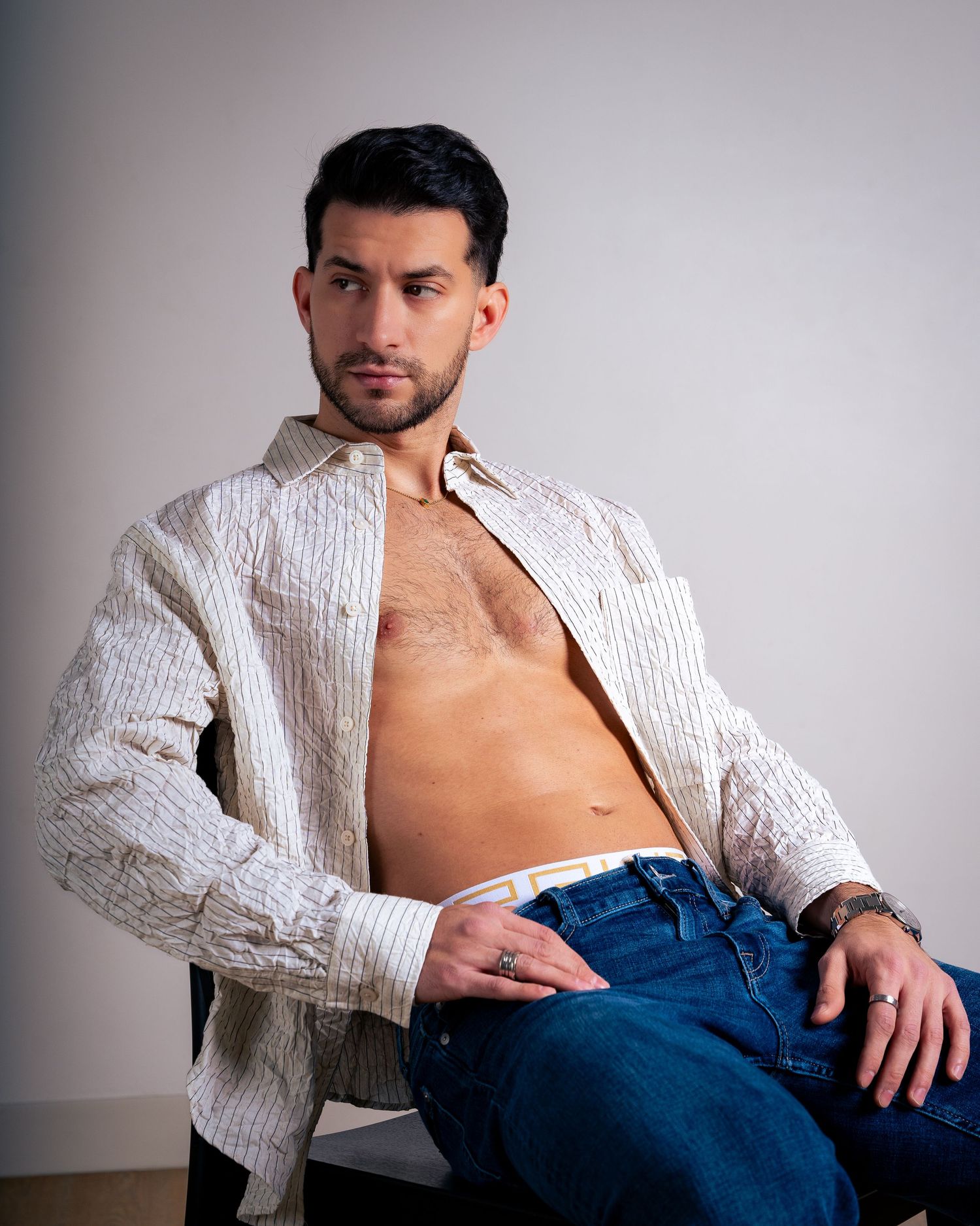 Model in white textured shirt and jeans poses against grey background in fashion photoshoot.
