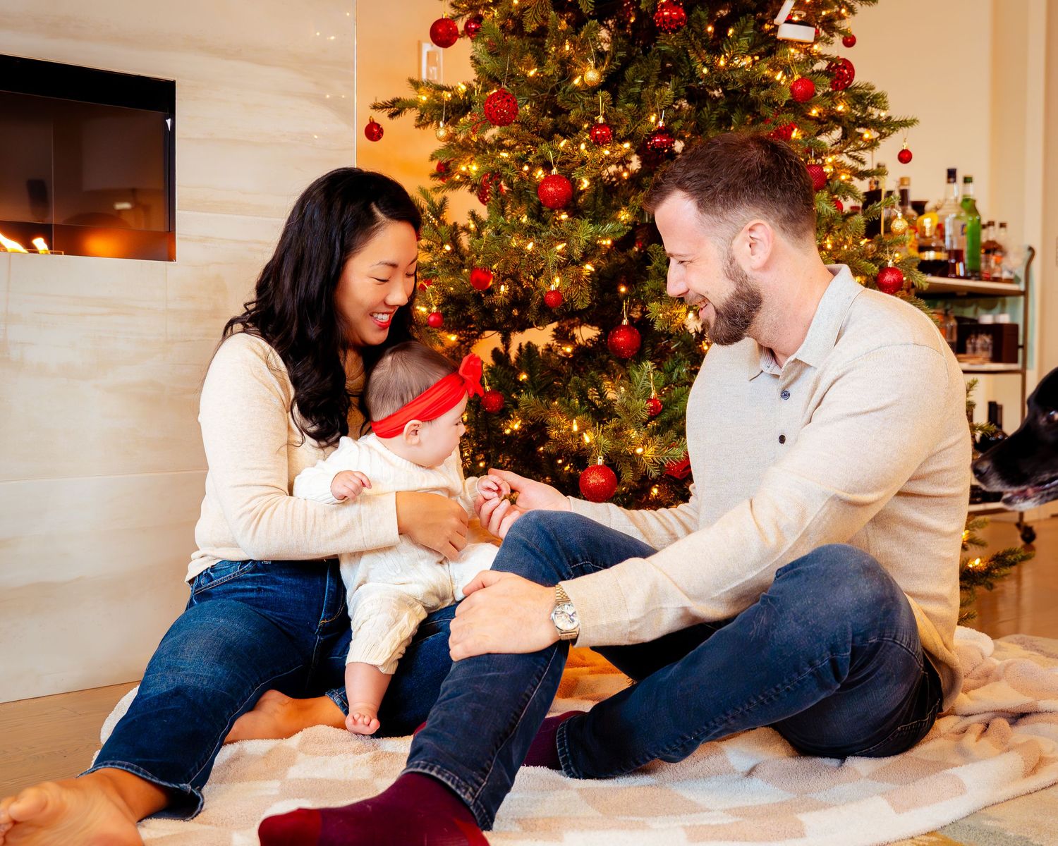 A family relaxes together on a couch near a decorated Christmas tree in a cozy living room.