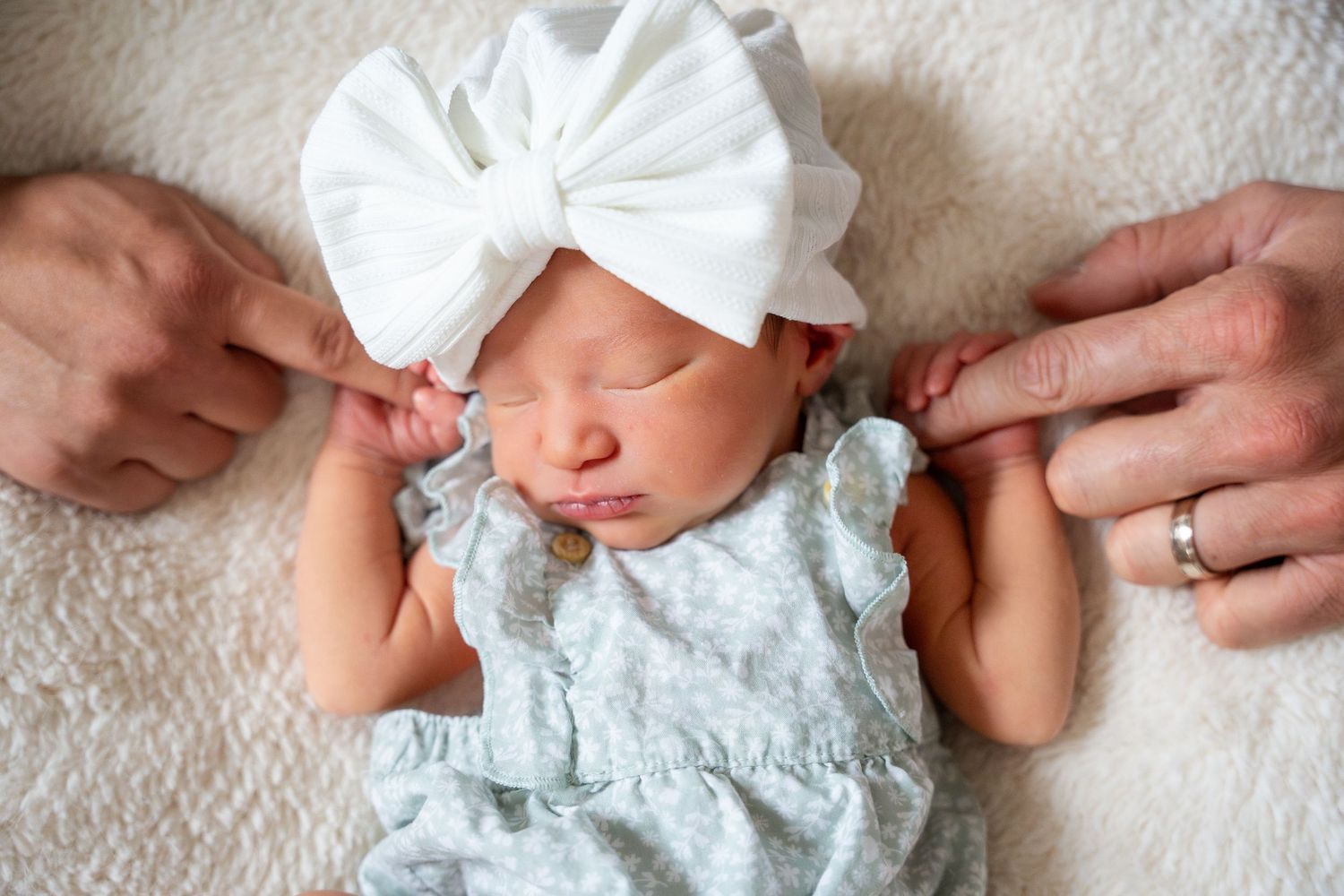 Infant in delicate white lace dress resting on plush cream carpet.