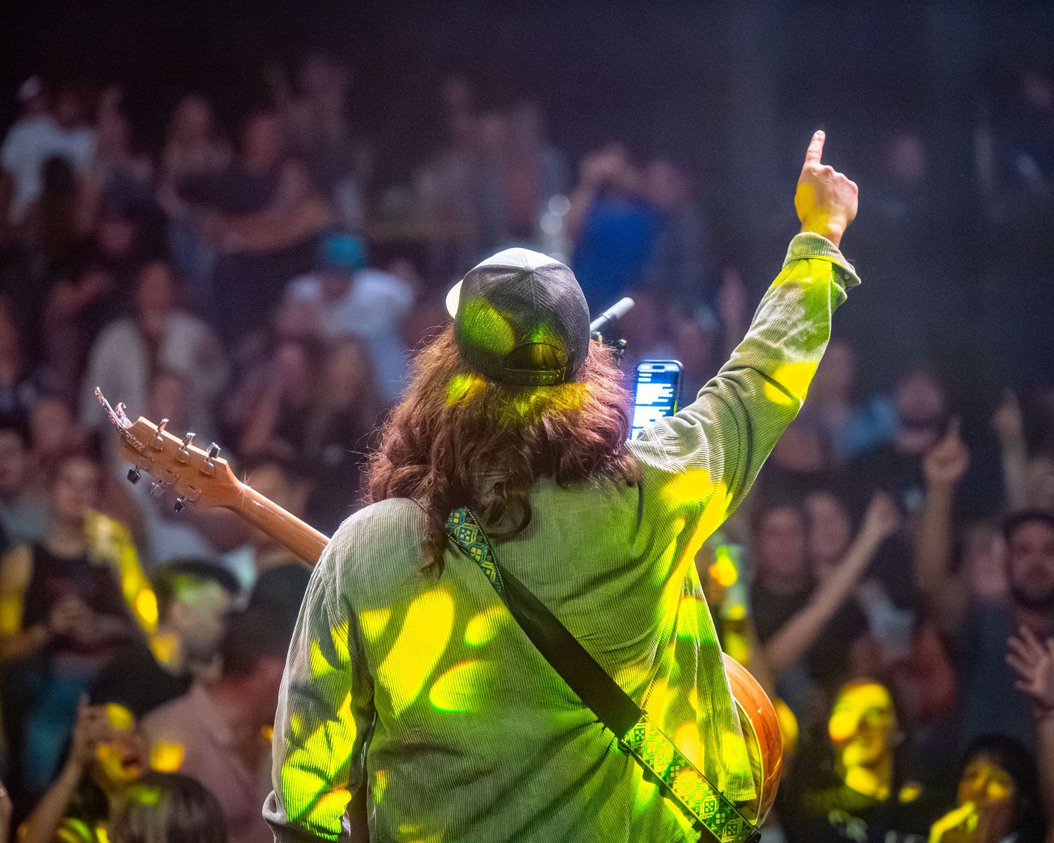 Performer in bright yellow attire energetically entertaining a large concert crowd.