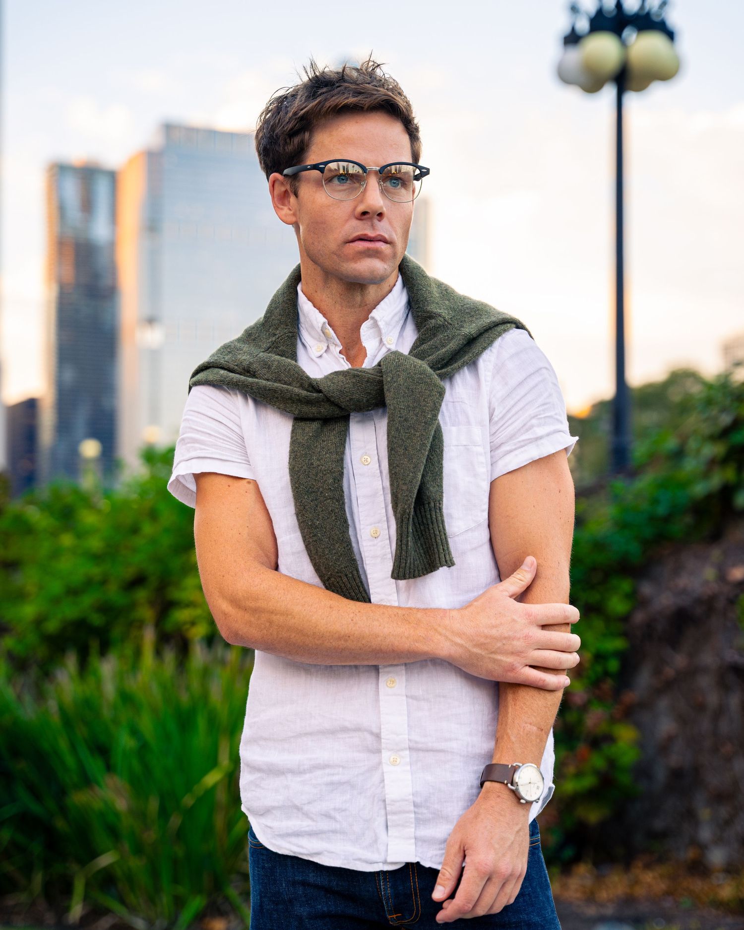 Summer casual look with white button-down shirt and olive sweater tied around shoulders.