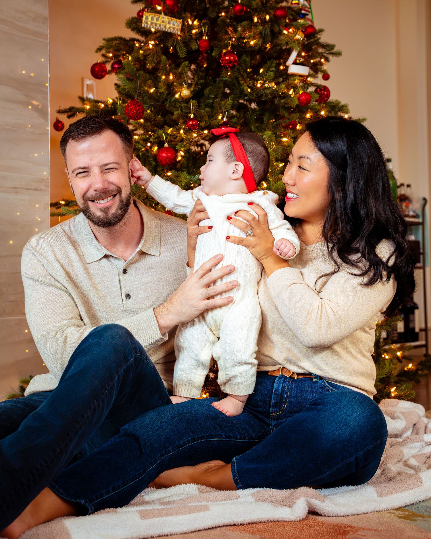 Family shares tender holiday moments together in front of decorated Christmas tree in warm living room setting.